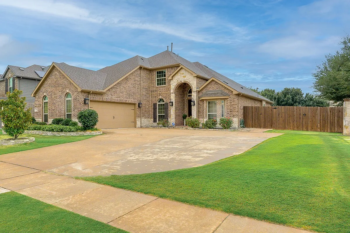 Brick exterior with stone accents, arched windows, an attached two-car garage, mature landscaping, and a fenced side yard