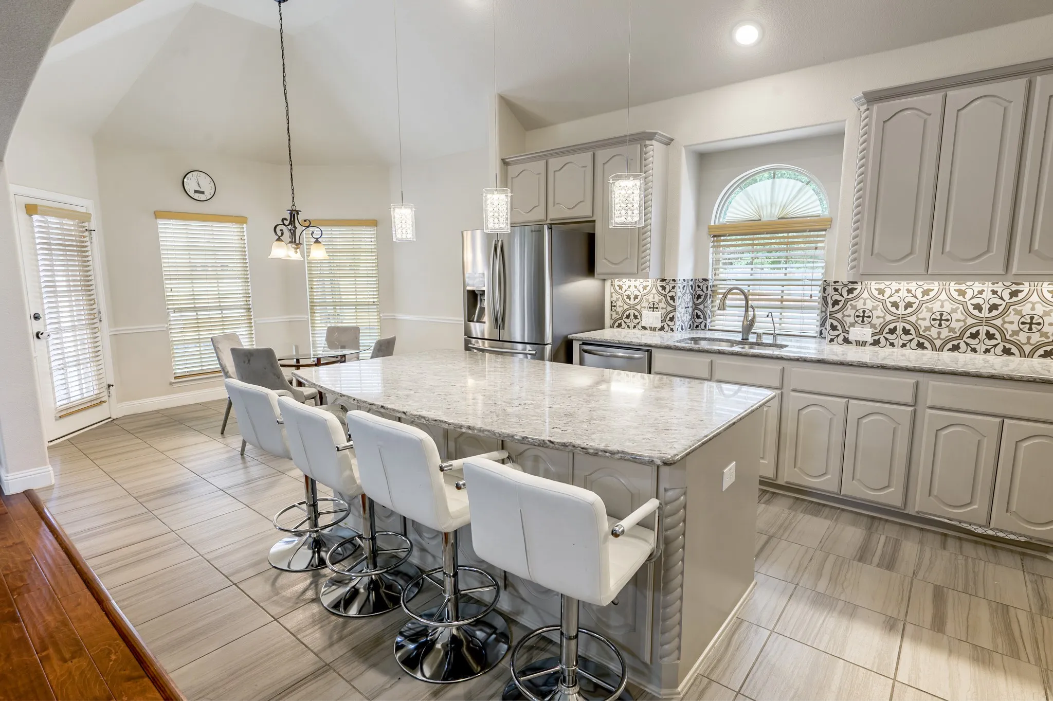 Kitchen with grey cabinetry, patterned backsplash, stainless steel appliances, and a central island with a light-toned countertop