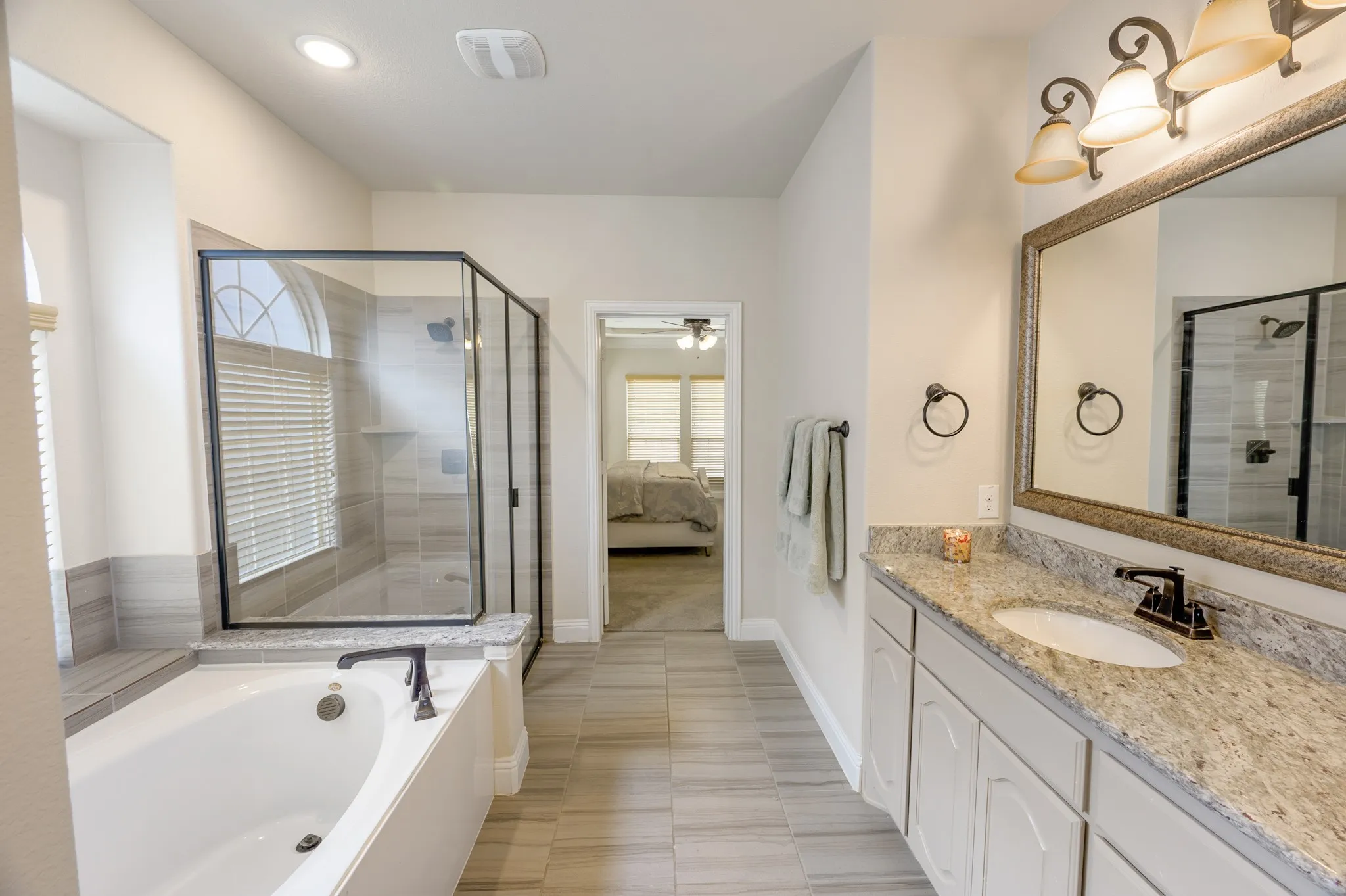 Spacious bathroom featuring a built-in bathtub, glass-enclosed shower, a vanity with a single basin, and wood-finish tile flooring