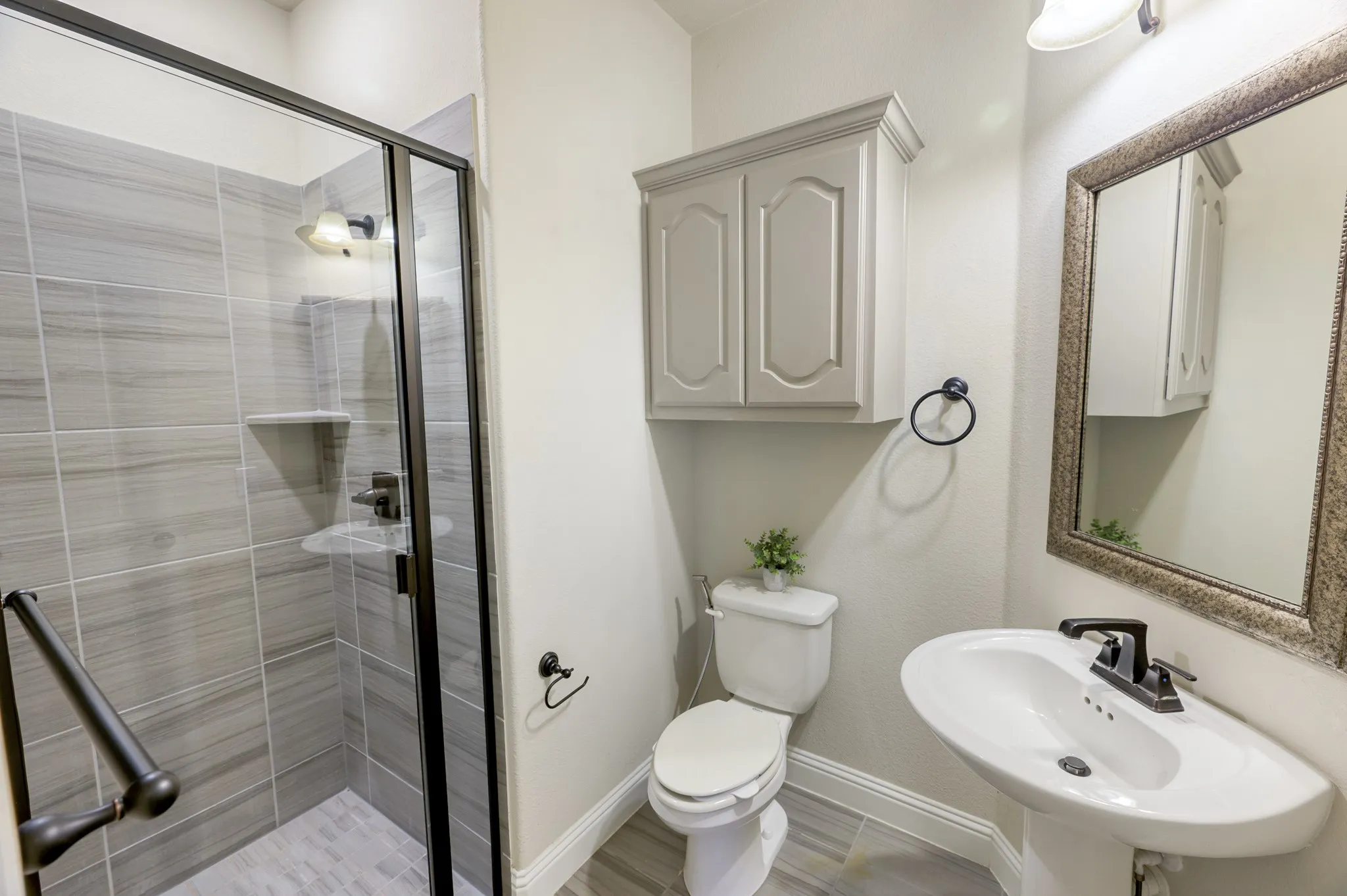 Walk-in shower with glass enclosure, pedestal sink, wall-mounted cabinetry, and tile flooring