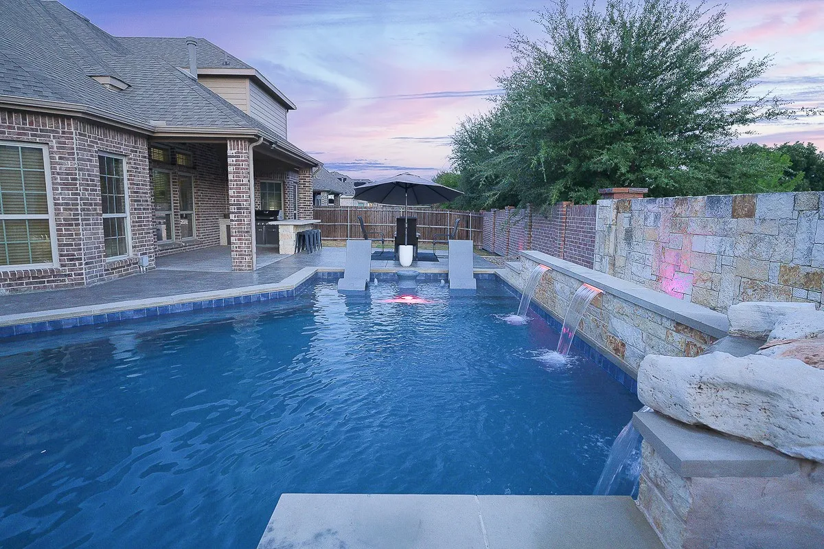 Brick and stone exterior with a covered patio, outdoor kitchen, and built-in swimming pool