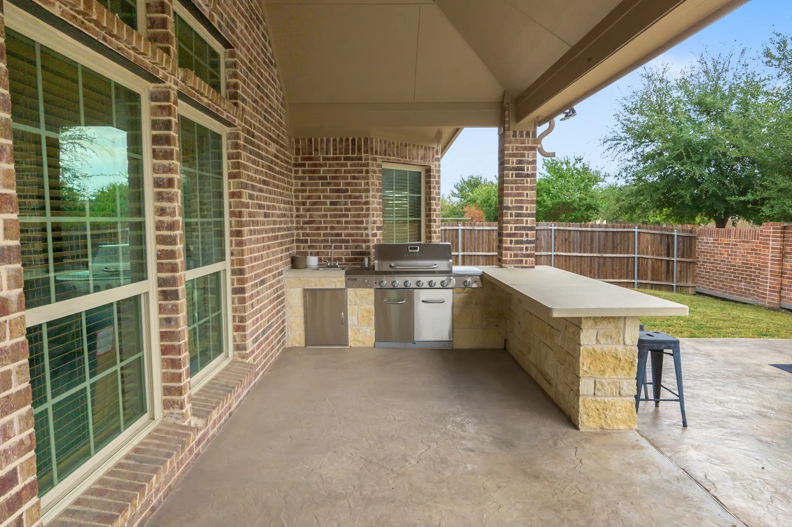 Covered patio featuring an outdoor kitchen with built-in grill, stone-clad bar, and stamped concrete flooring
