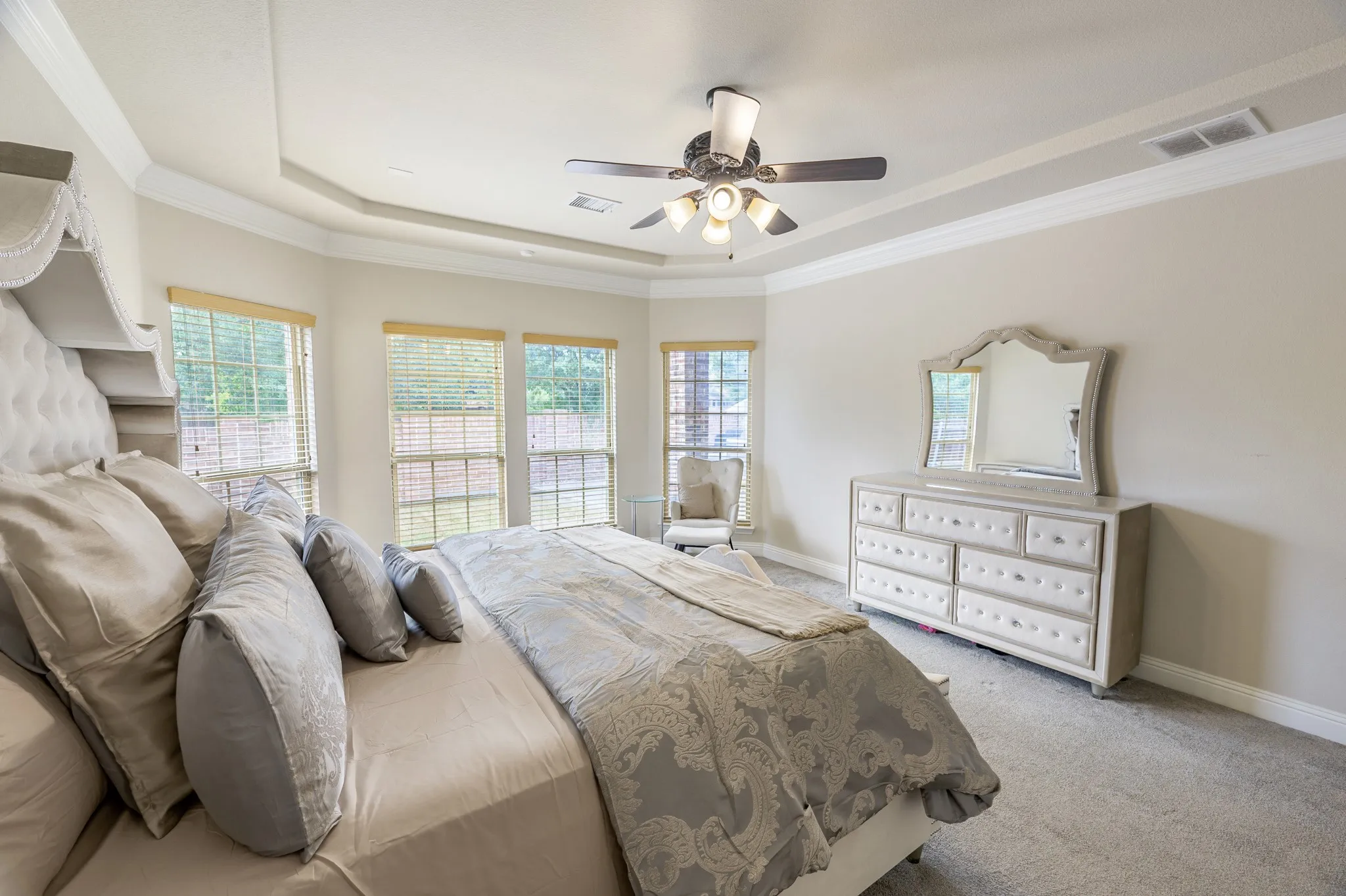 Tray ceiling with crown molding, ceiling fan with integrated lighting, multiple windows with blinds, and neutral carpeting