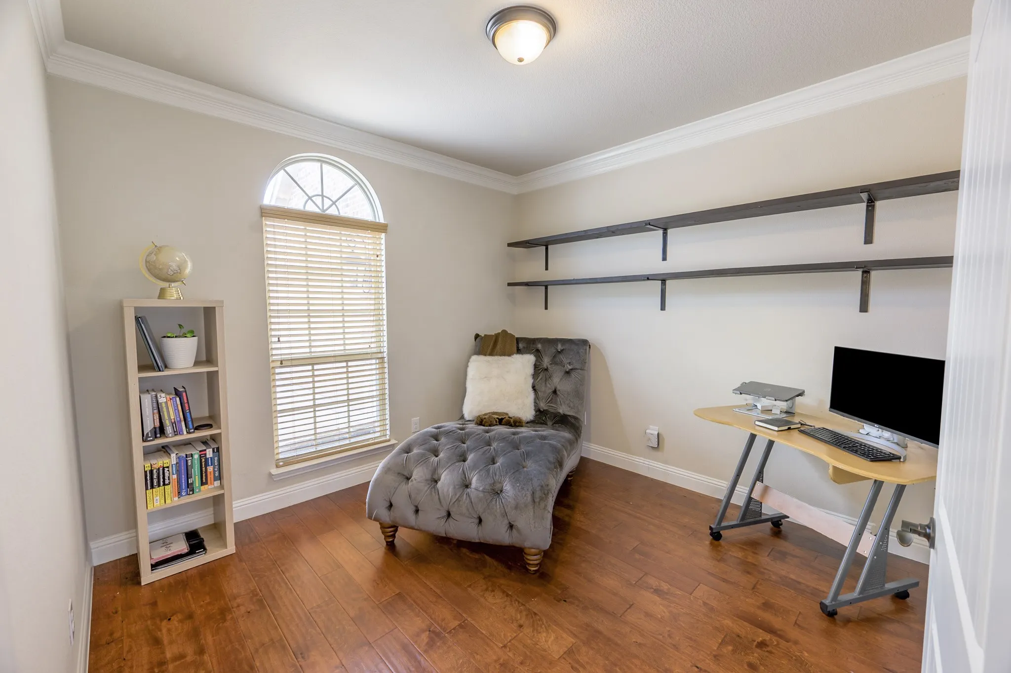 Room featuring wood-finish flooring, crown molding, an arched window, and built-in wall shelving