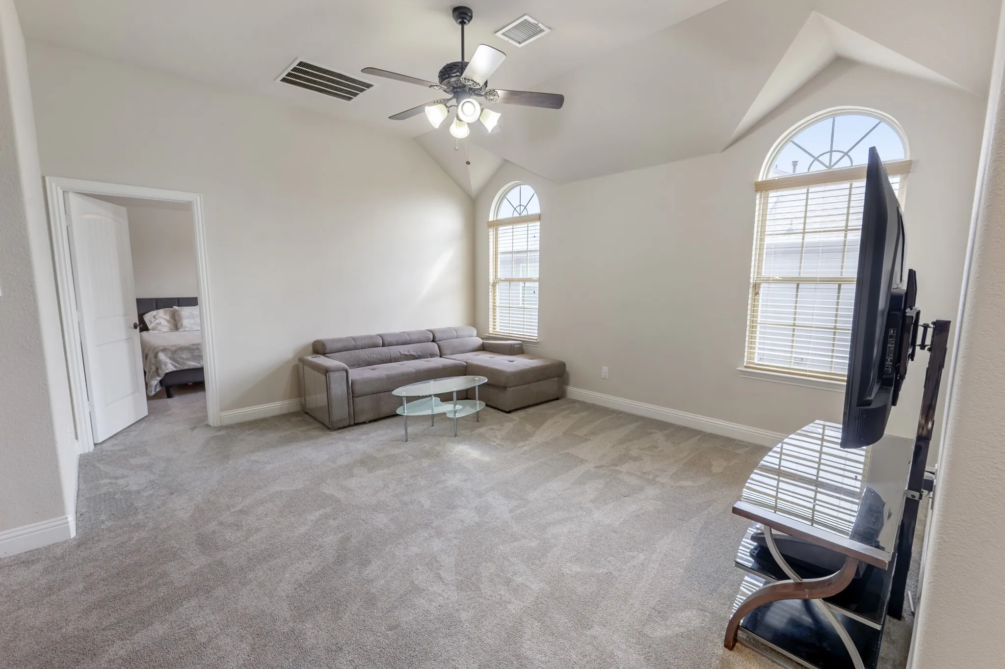 Vaulted ceiling with a ceiling fan, arched windows, light-colored carpeting, and a paneled interior door