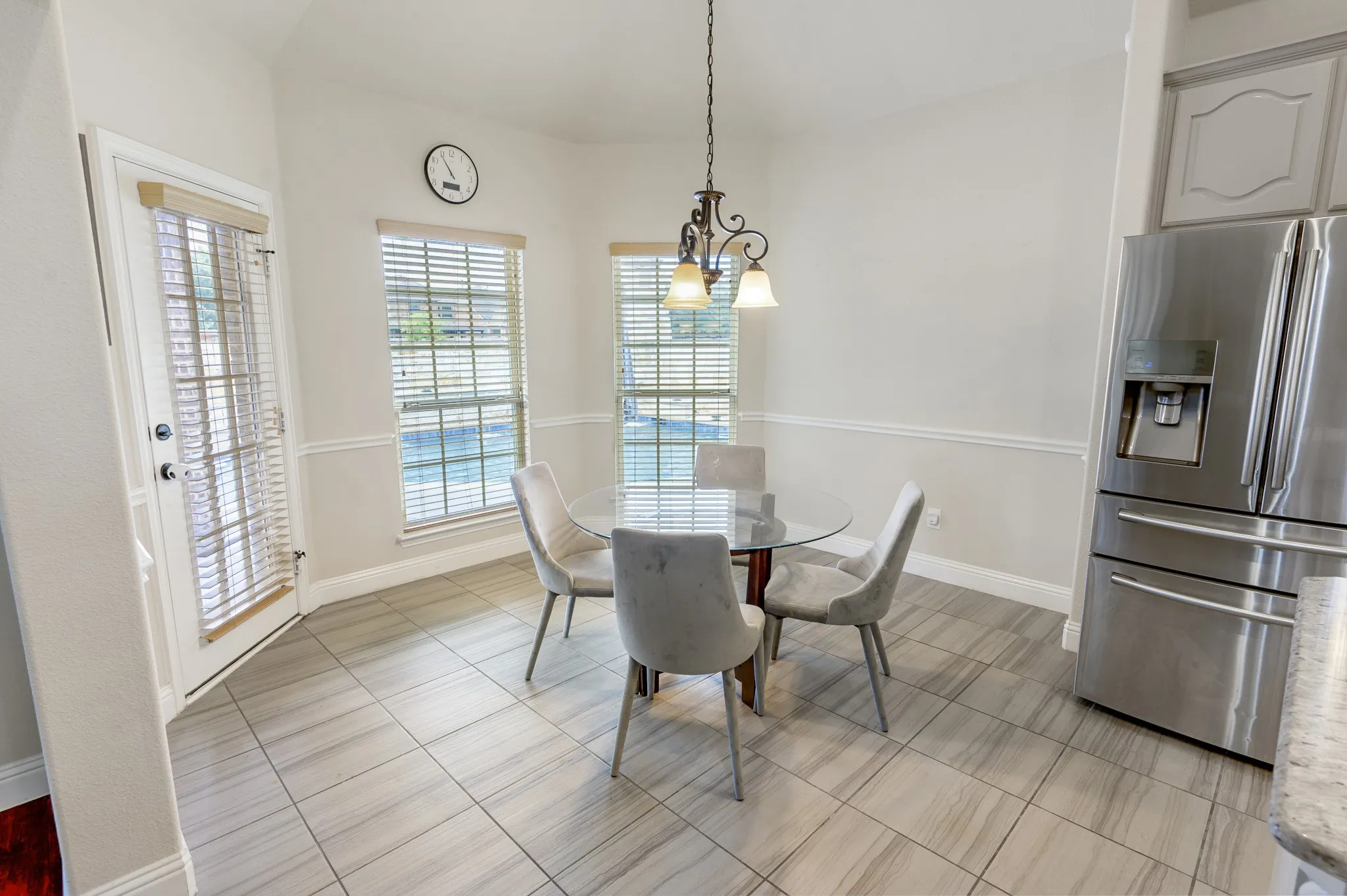 Stainless steel refrigerator, tile flooring, built-in wall paneling, chandelier, and multiple windows
