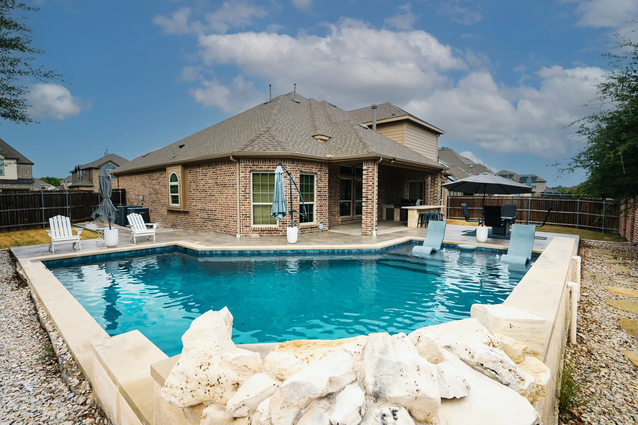 Expansive backyard featuring a custom-shaped inground pool, a covered patio, and a brick exterior