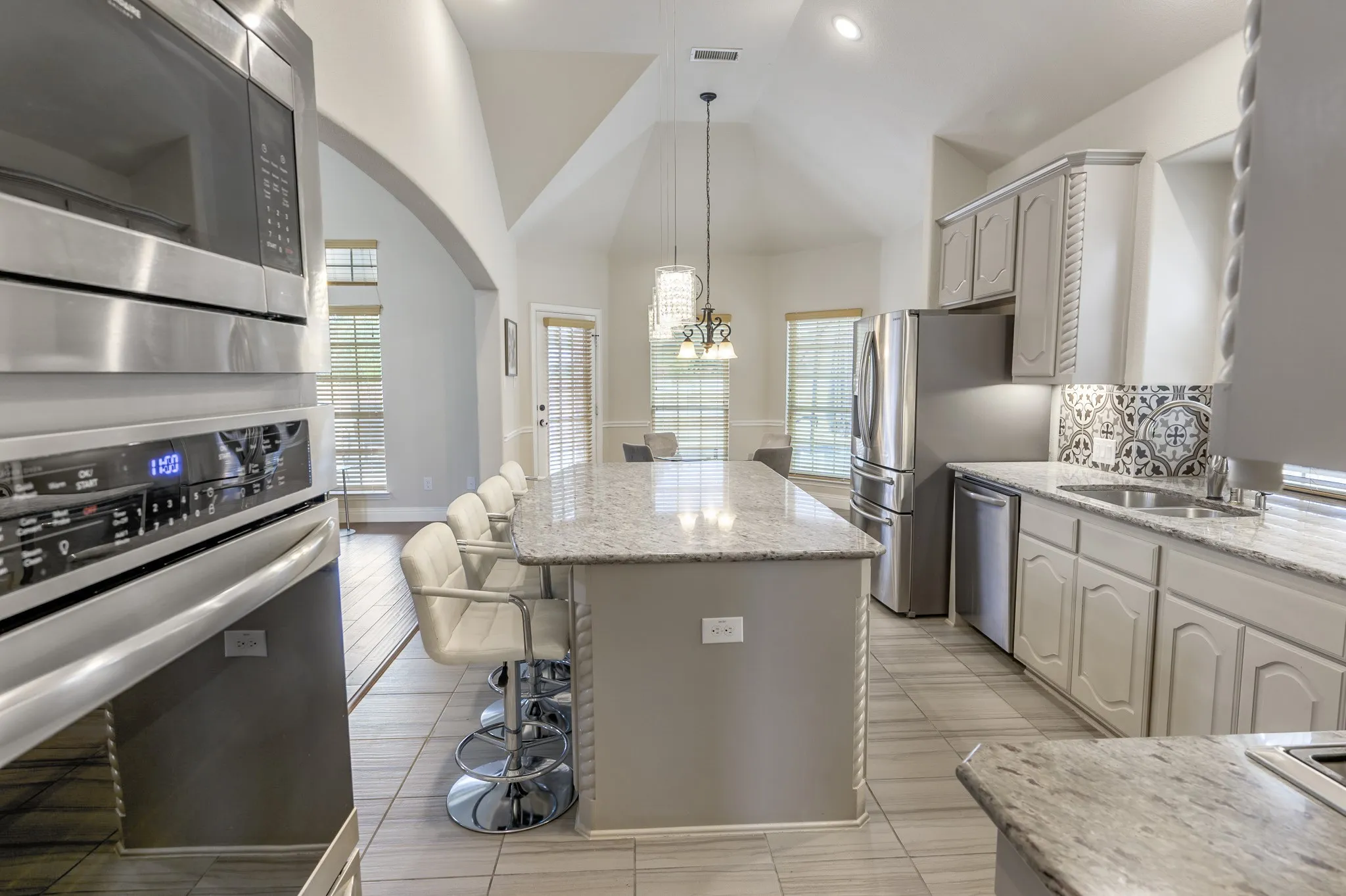 Kitchen featuring a large island with seating, stainless steel appliances, light-toned cabinetry, patterned tile backsplash, and vaulted ceilings