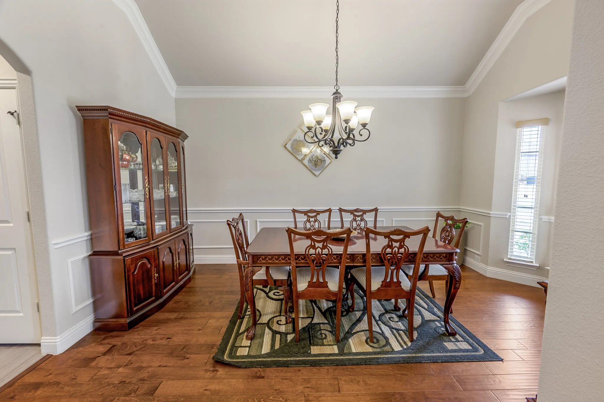 Wood-finish flooring, crown molding, chair rail molding, and a chandelier lighting fixture