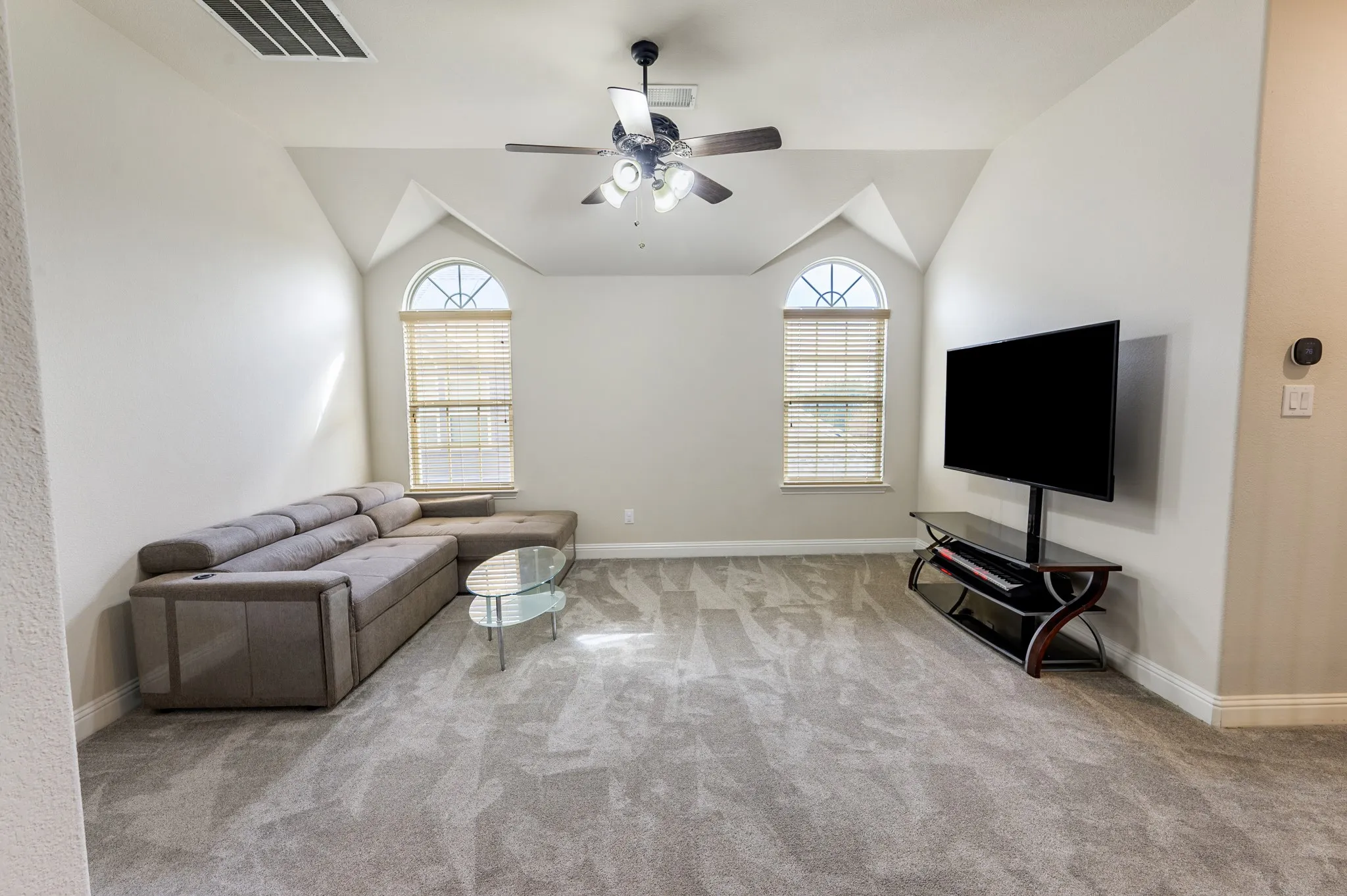 Room featuring vaulted ceilings with arched window accents, a ceiling fan with integrated lighting, and neutral carpeting
