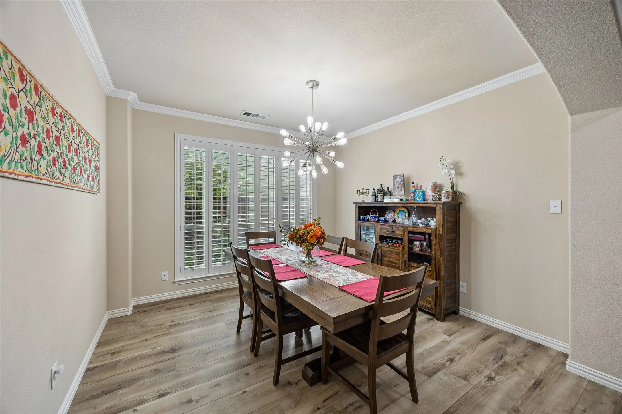 Wood-finish flooring with crisp white baseboards, crown molding, and a modern chandelier