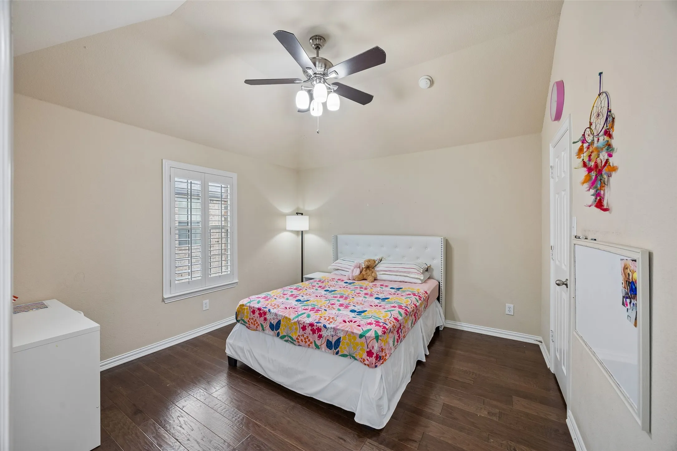 Vaulted ceiling with a ceiling fan, wood-finish flooring, white window shutters, and a white door