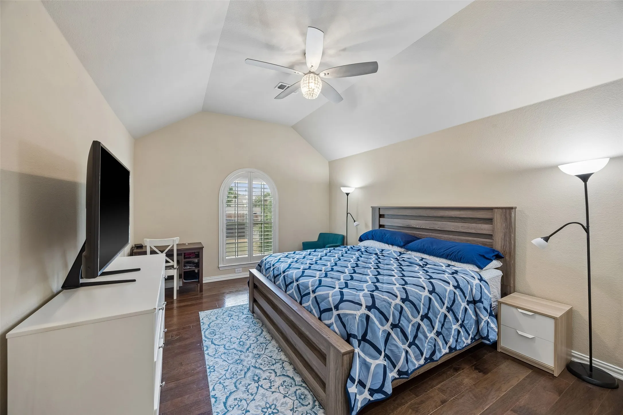 Vaulted ceiling with a ceiling fan, arched window with plantation shutters, wood-finish flooring, and neutral wall tones