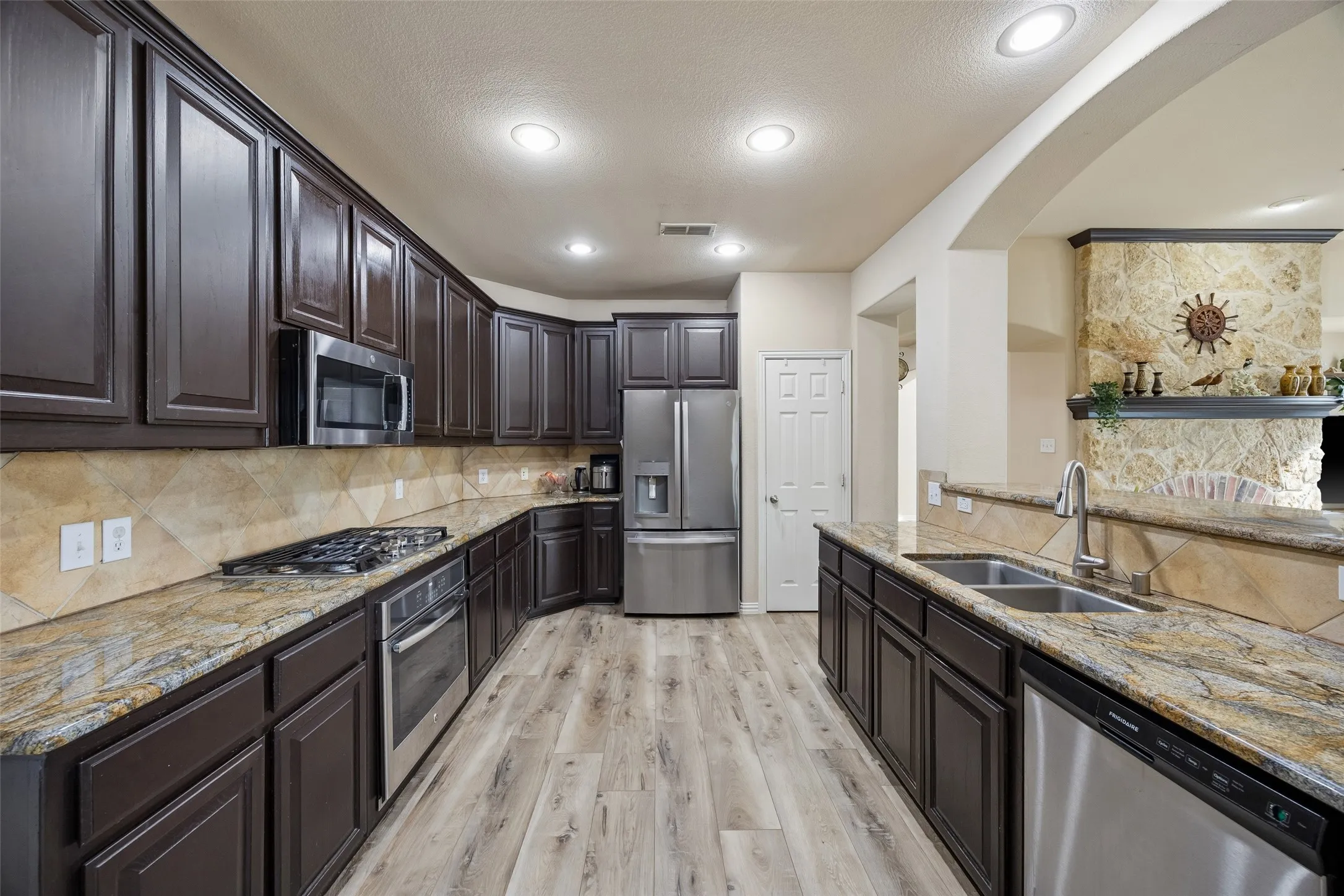 Kitchen featuring wood-finish flooring, dark wood cabinetry, stainless steel appliances, granite countertops, and recessed lighting