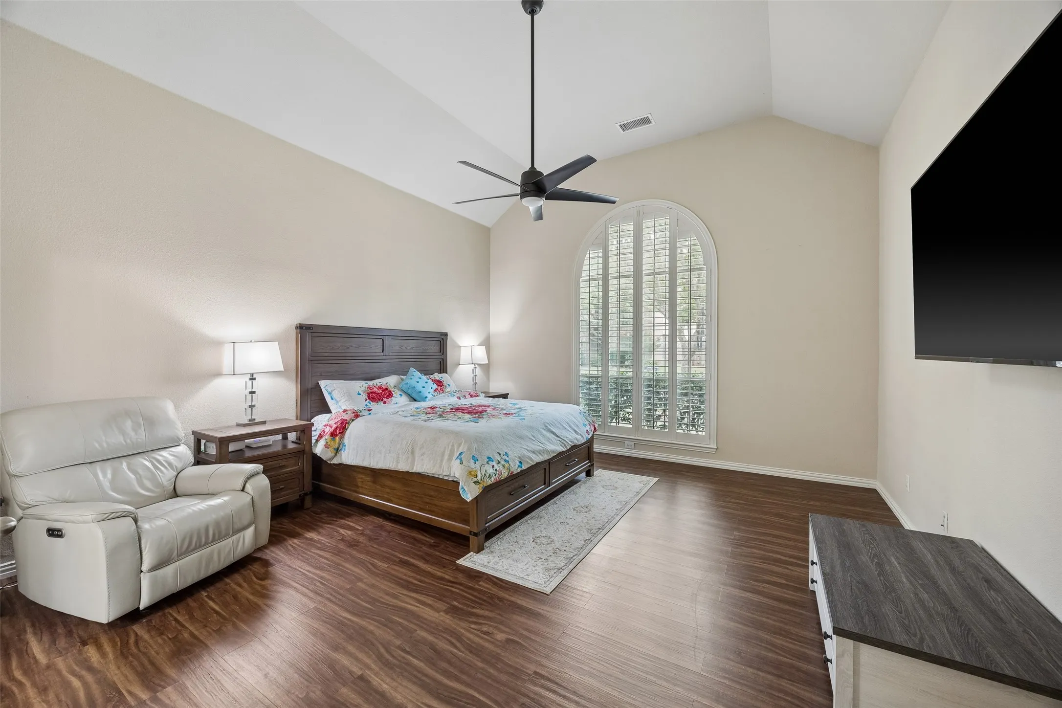 Vaulted ceiling with a ceiling fan, arched window with plantation shutters, wood-finish flooring, and neutral wall paint