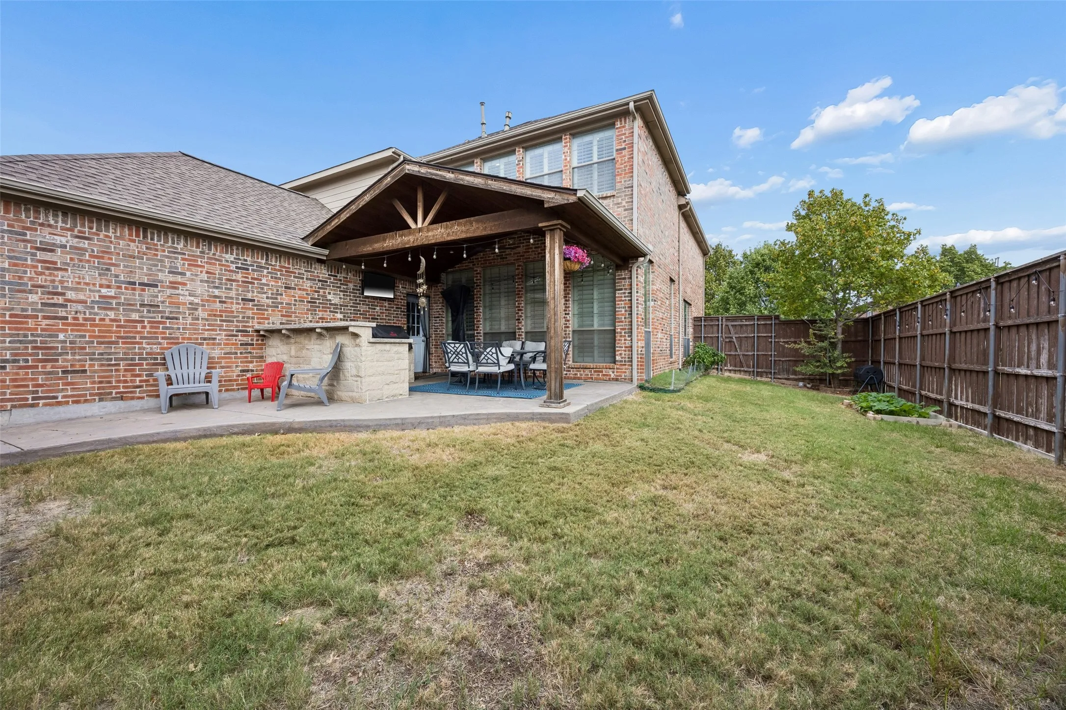 Brick exterior, covered patio, outdoor kitchen area, fenced yard, and concrete patio