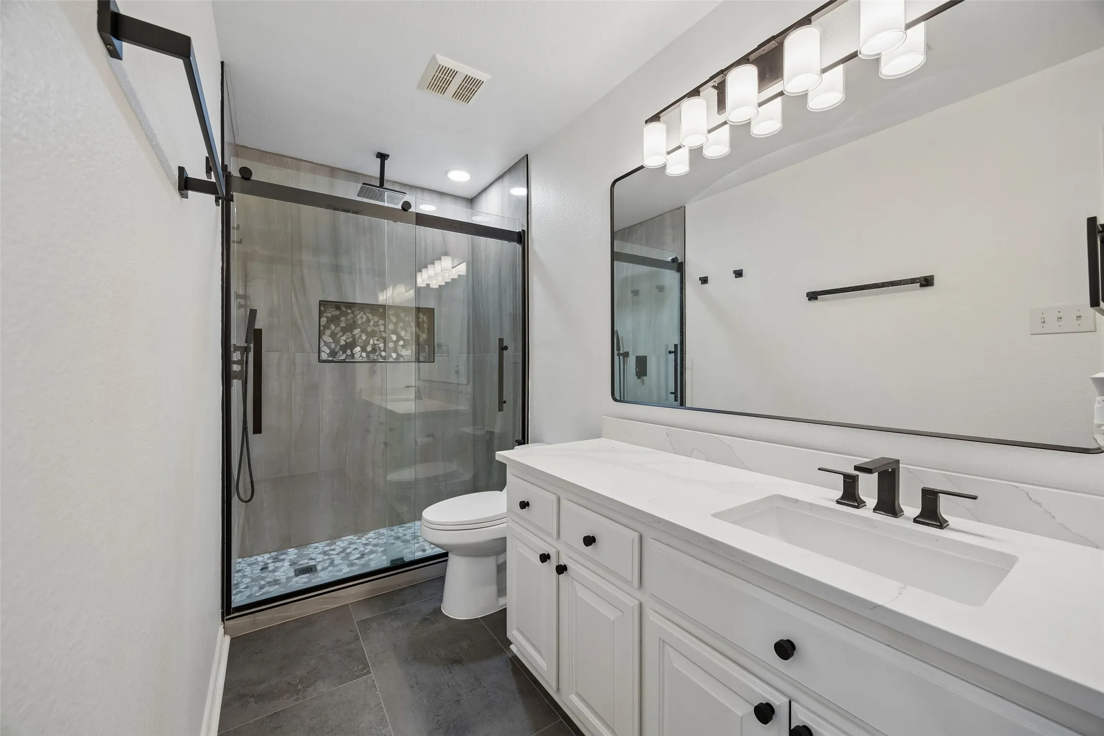 Spacious bathroom featuring a frameless glass shower, built-in shower niche, floating vanity with an integrated sink, and an expansive mirror