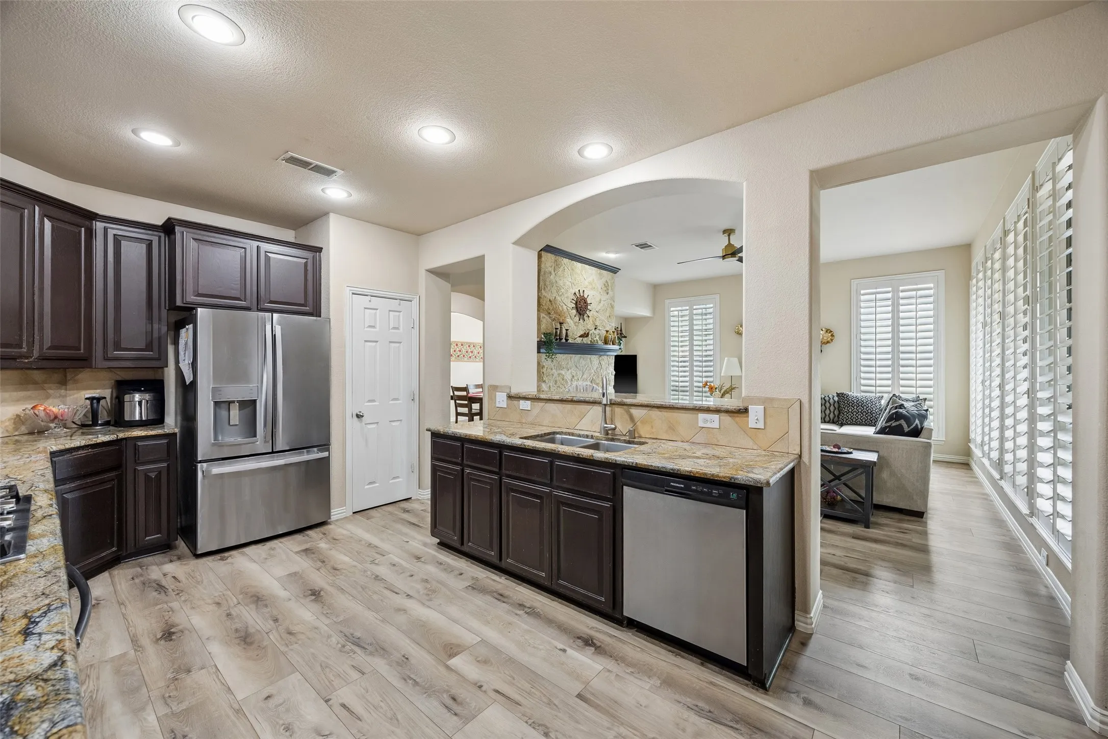 Kitchen featuring wood-finish flooring, dark wood cabinetry, stainless steel appliances, and stone countertops with a tile backsplash