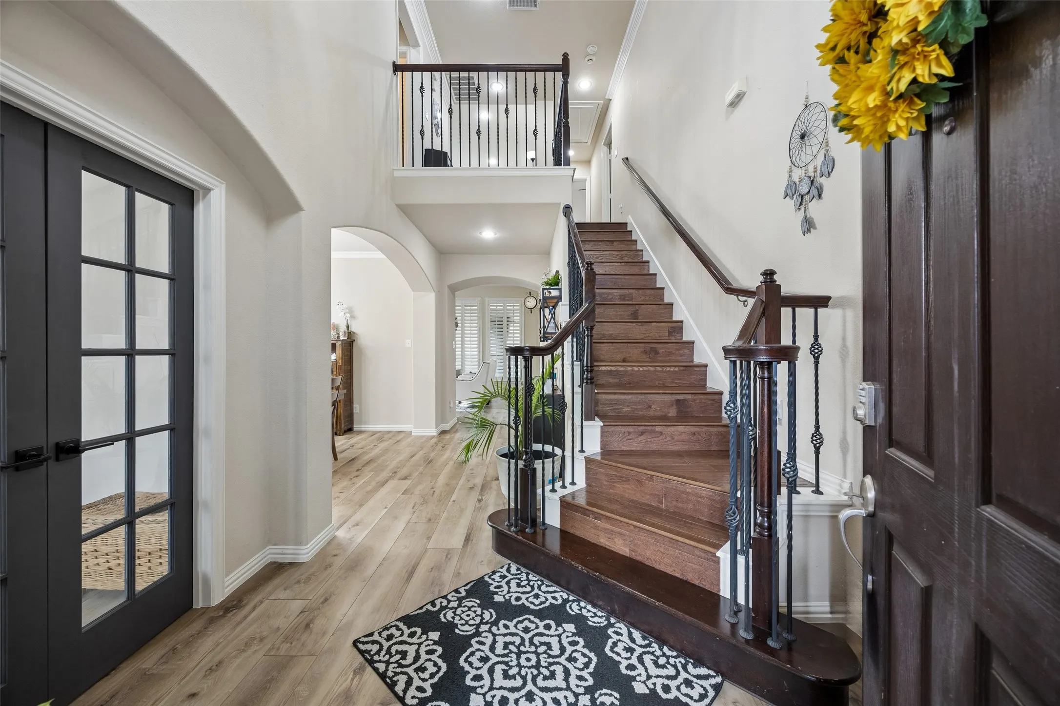 Wood-finish flooring throughout the entry, a dark wood staircase with wrought iron balusters, and a second-level landing with matching balusters