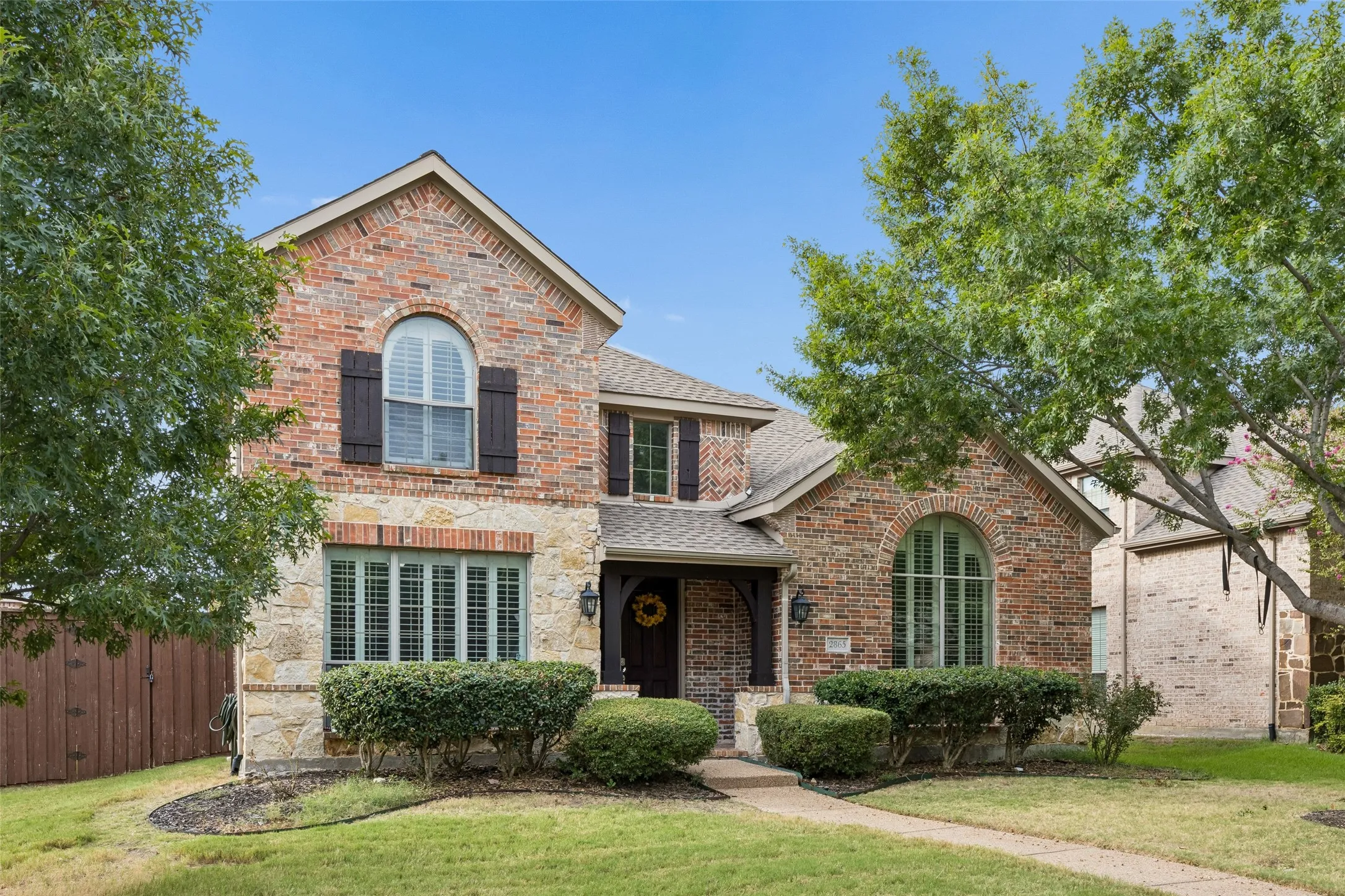 Brick and stone exterior with arched windows, dark shutters, and a covered entry