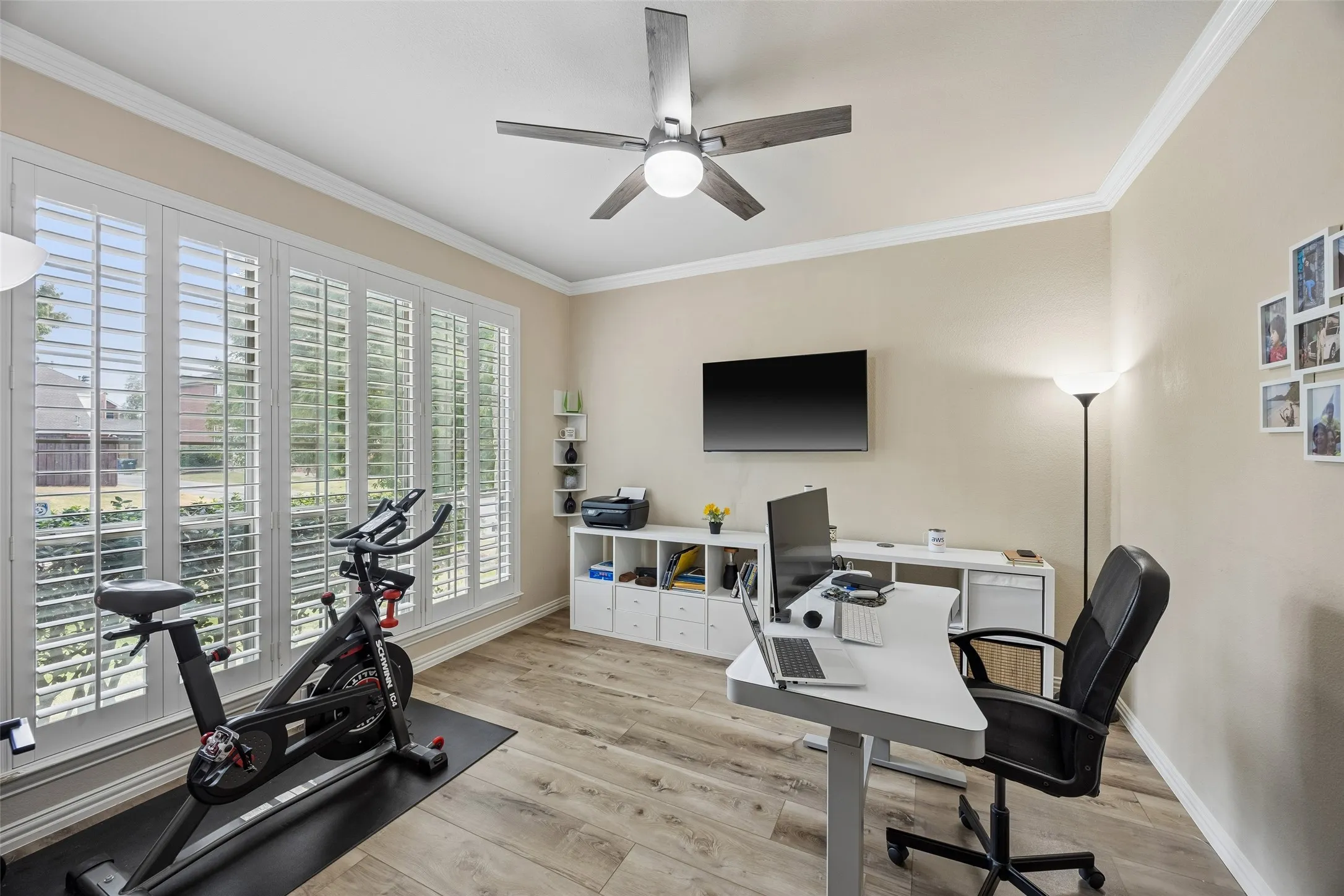 Light wood-finish flooring, white plantation shutters, and crown molding