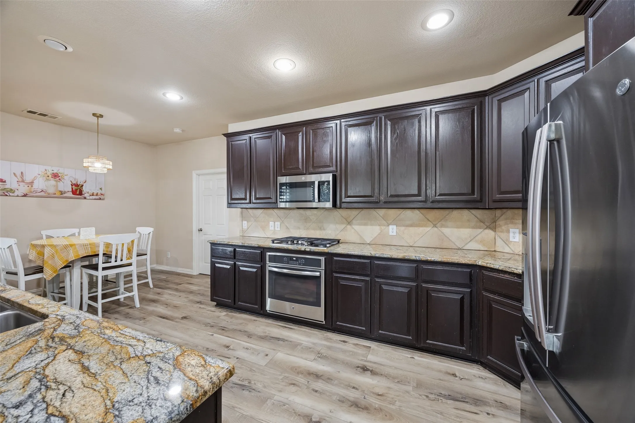 Kitchen featuring dark wood cabinetry, light-toned countertops, a diagonal tile backsplash, stainless steel appliances, and wood-finish flooring