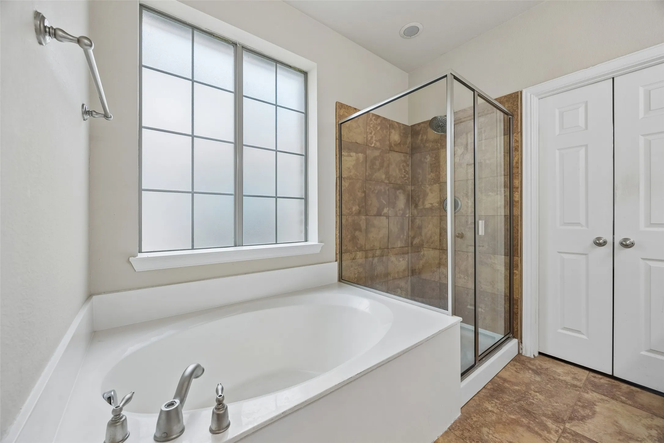 Built-in soaking tub, glass-enclosed shower with tile surround, privacy window, and wood-finish flooring