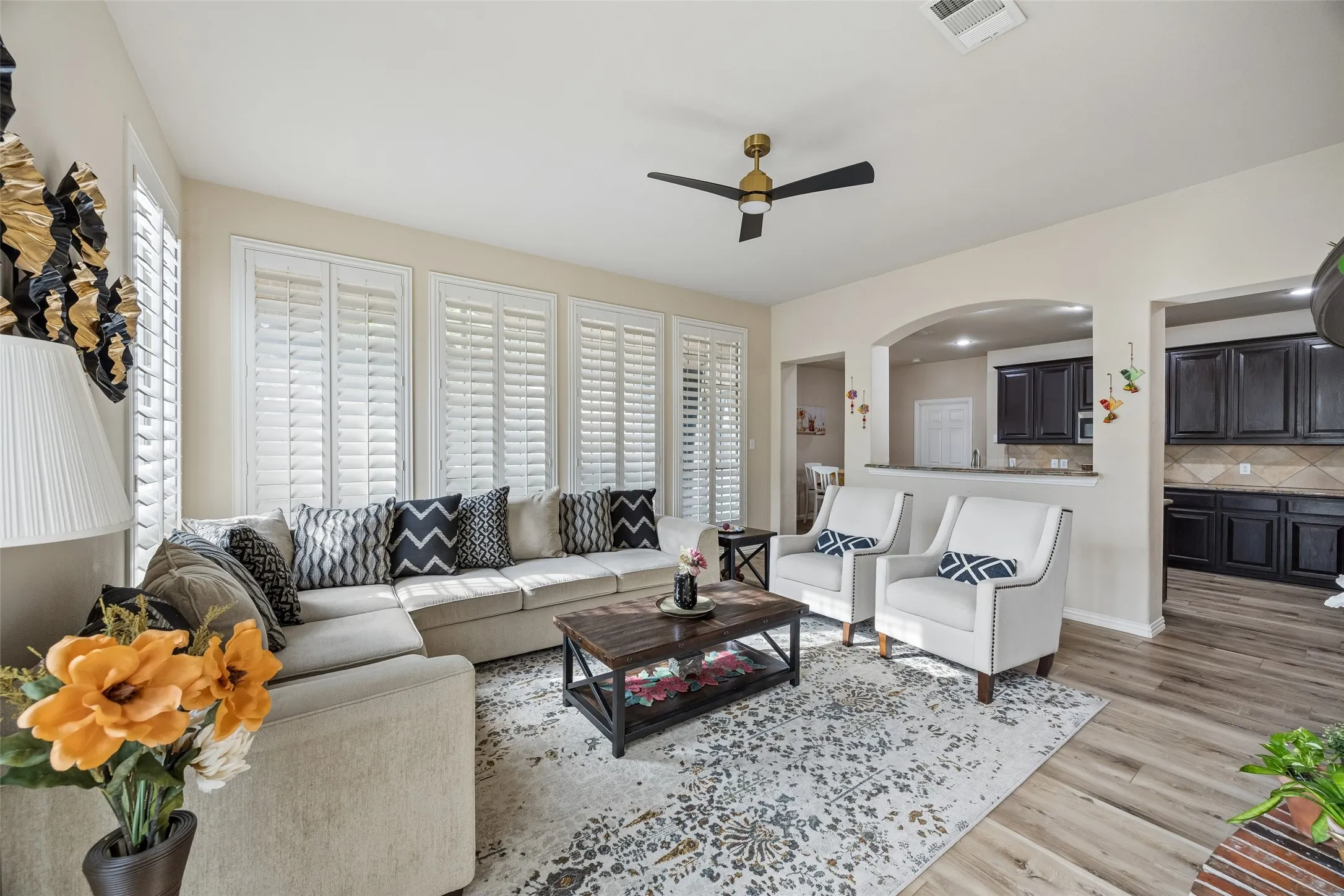 Spacious living area featuring plank flooring, multiple windows with plantation shutters, and a modern ceiling fan