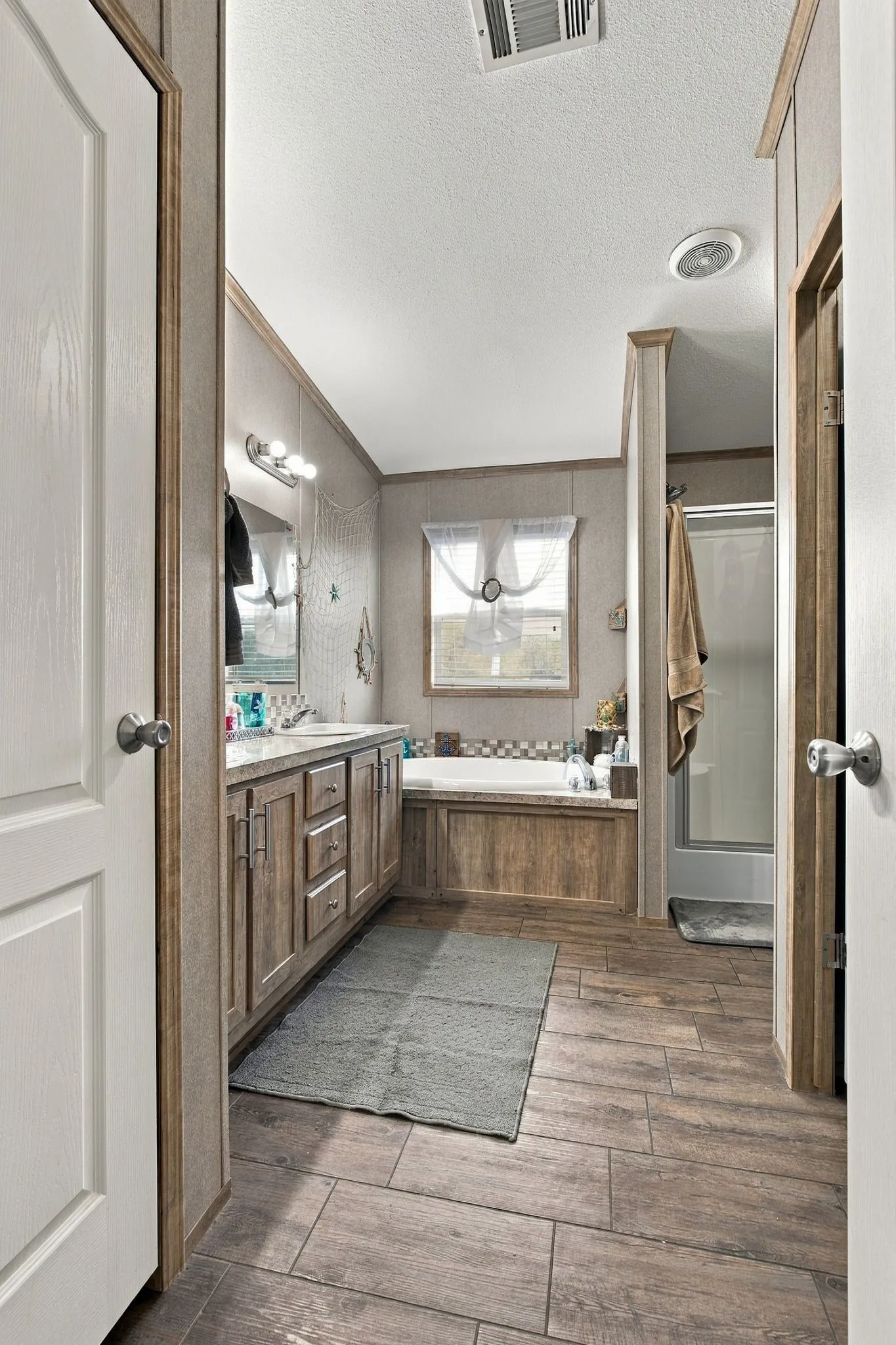 Wood-finish plank tile flooring, double vanity with base cabinetry, built-in soaking tub, and a separate shower enclosure