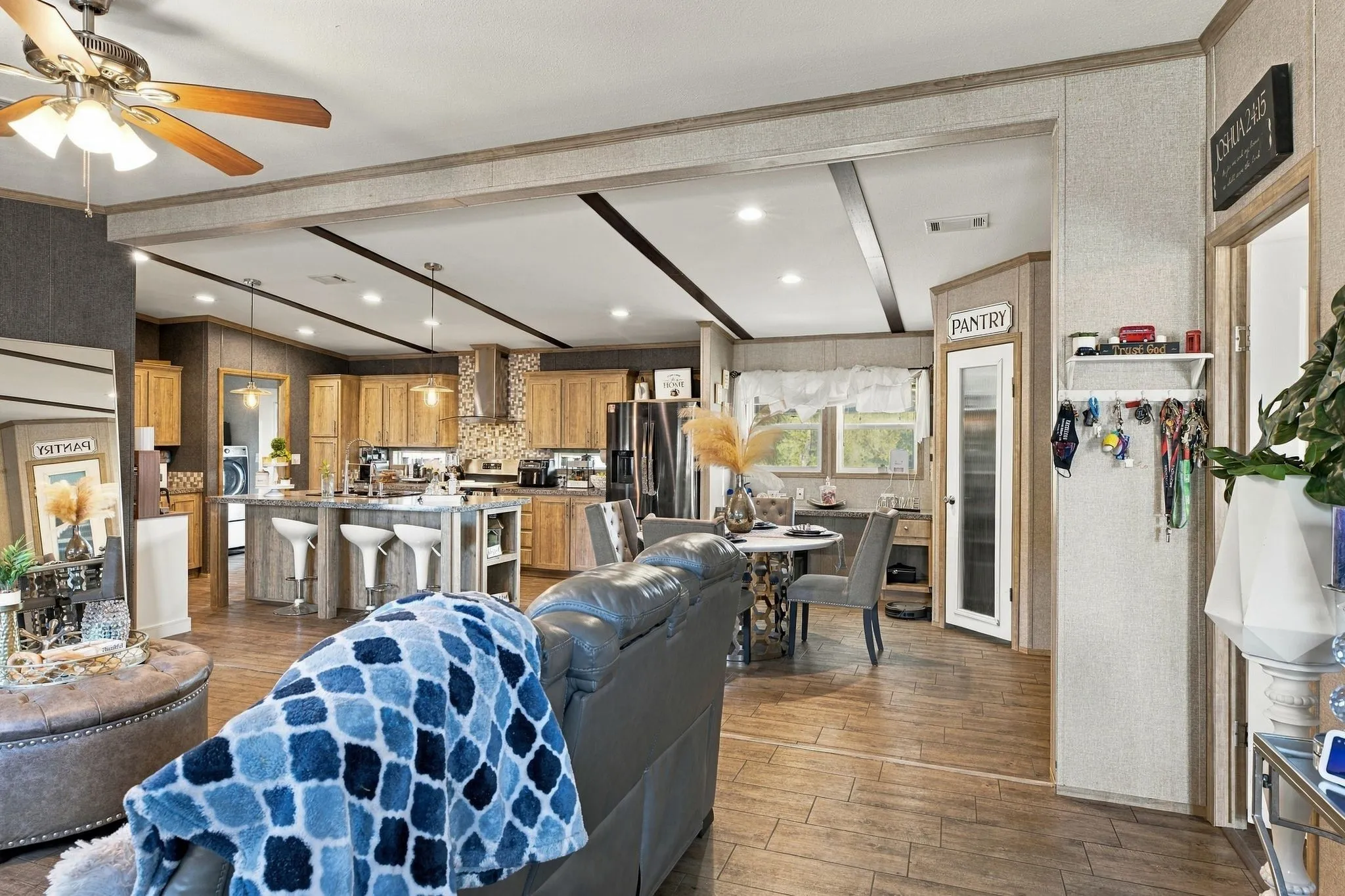 Open-concept living area with wood-finish flooring, a kitchen featuring wood cabinetry and a tile backsplash, and a dedicated pantry