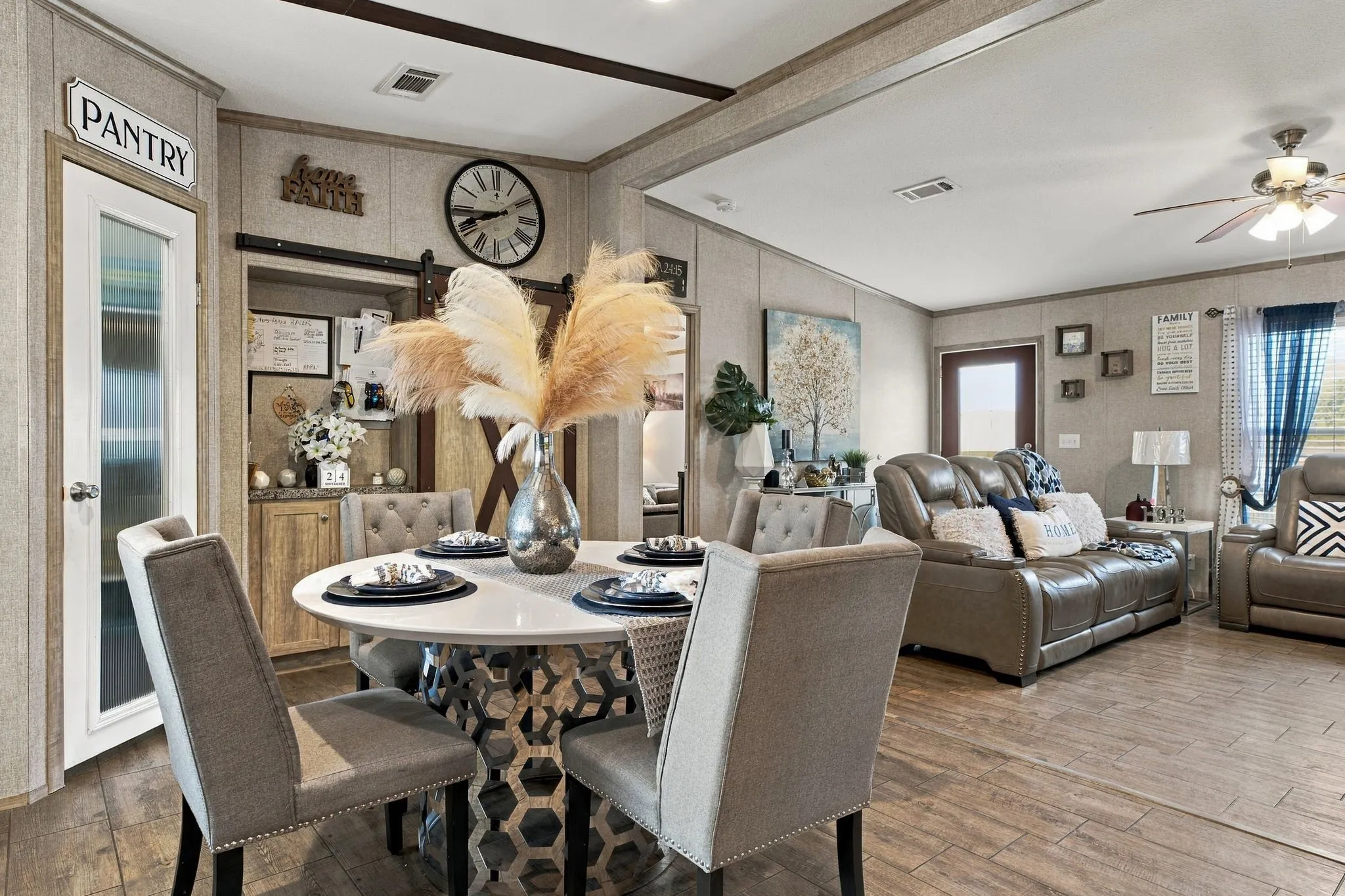 Open-concept living space with wood-finish flooring, a contemporary dining table, a pantry door with a frosted glass panel, and a ceiling fan