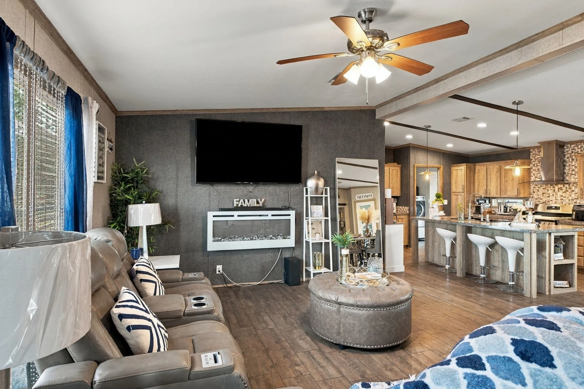Living area with wood-finish flooring, a ceiling fan, and a wall-mounted electric fireplace