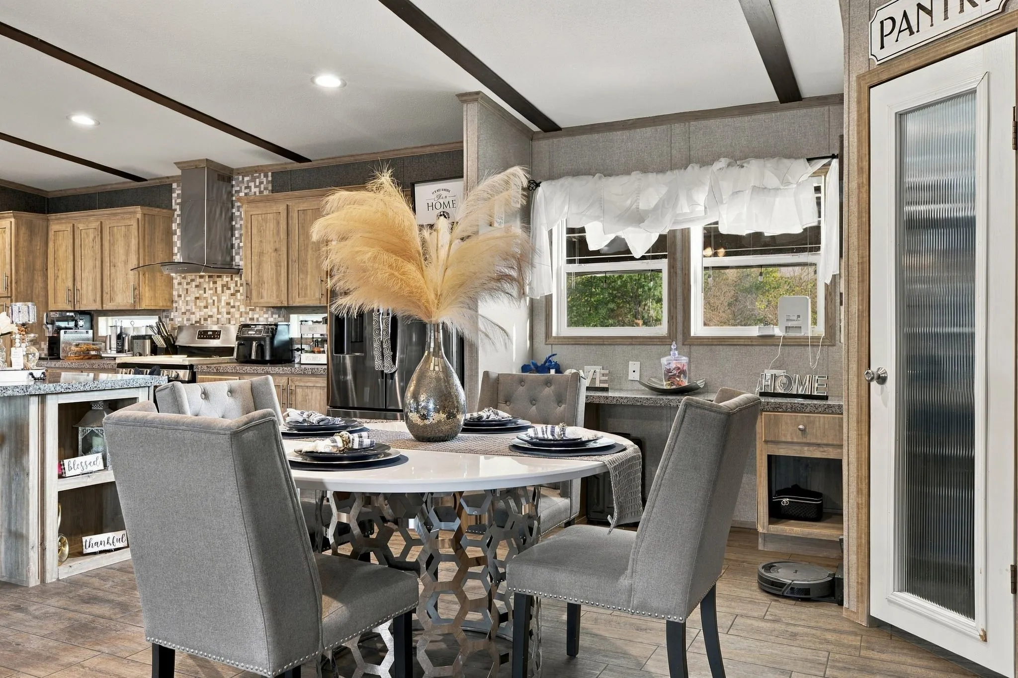 Kitchen and dining area featuring wood-finish cabinetry, stainless steel range hood, mosaic tile backsplash, and a built-in pantry with a fluted glass door