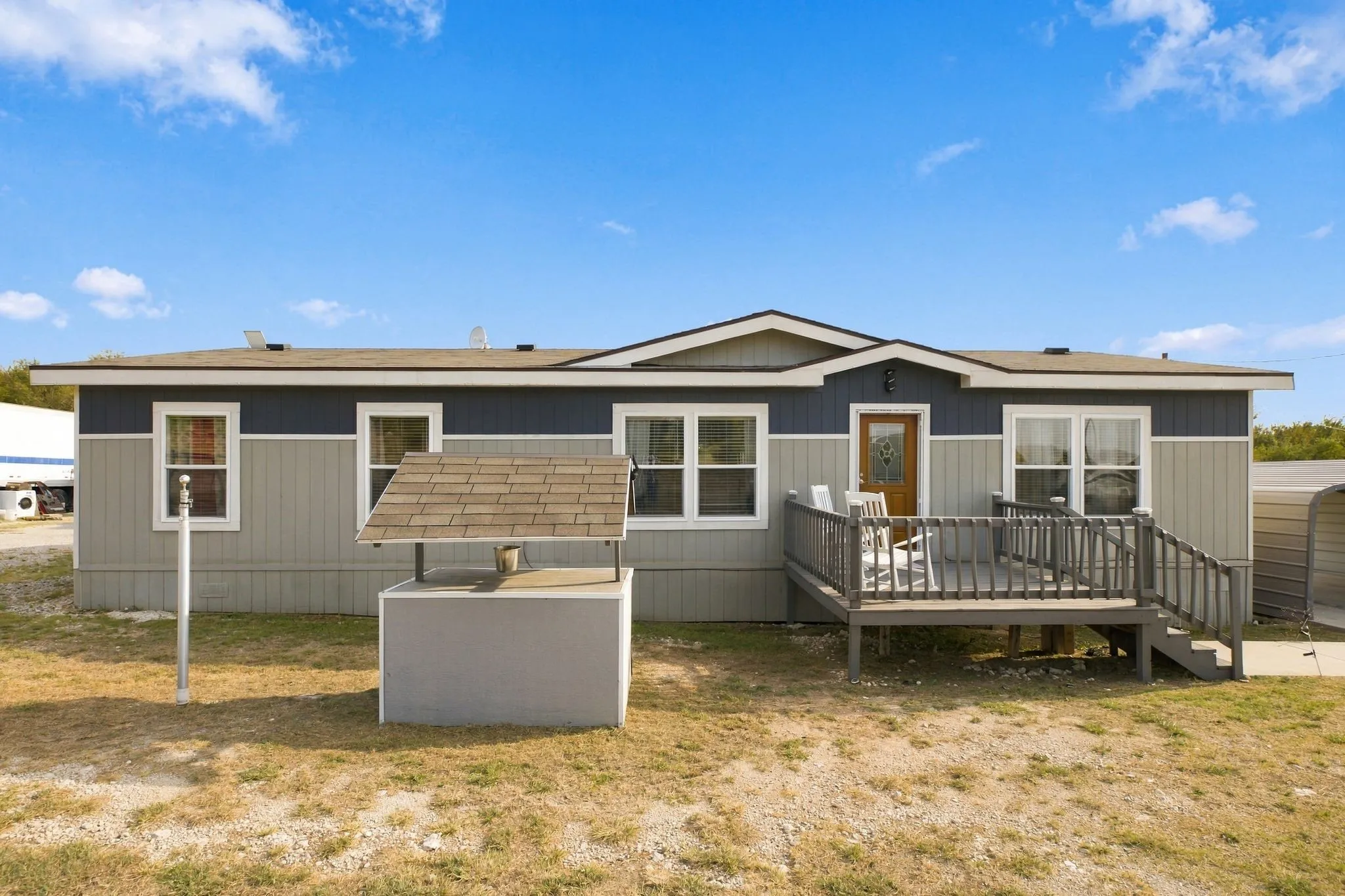 Two-tone exterior siding, front entry deck, wood-finish front door, multiple windows, and a decorative well structure