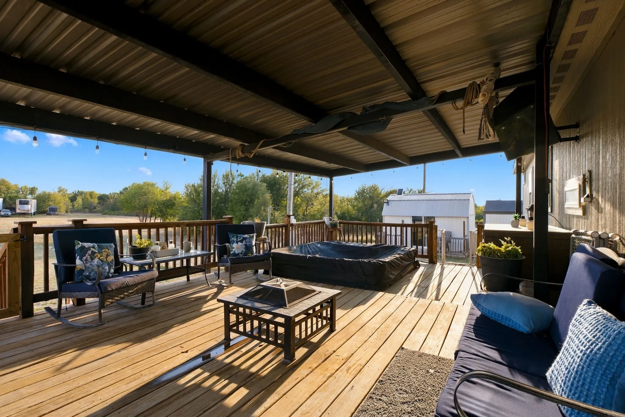 Expansive outdoor decking with a covered patio, wood railing, string lighting, and a dark-toned hot tub
