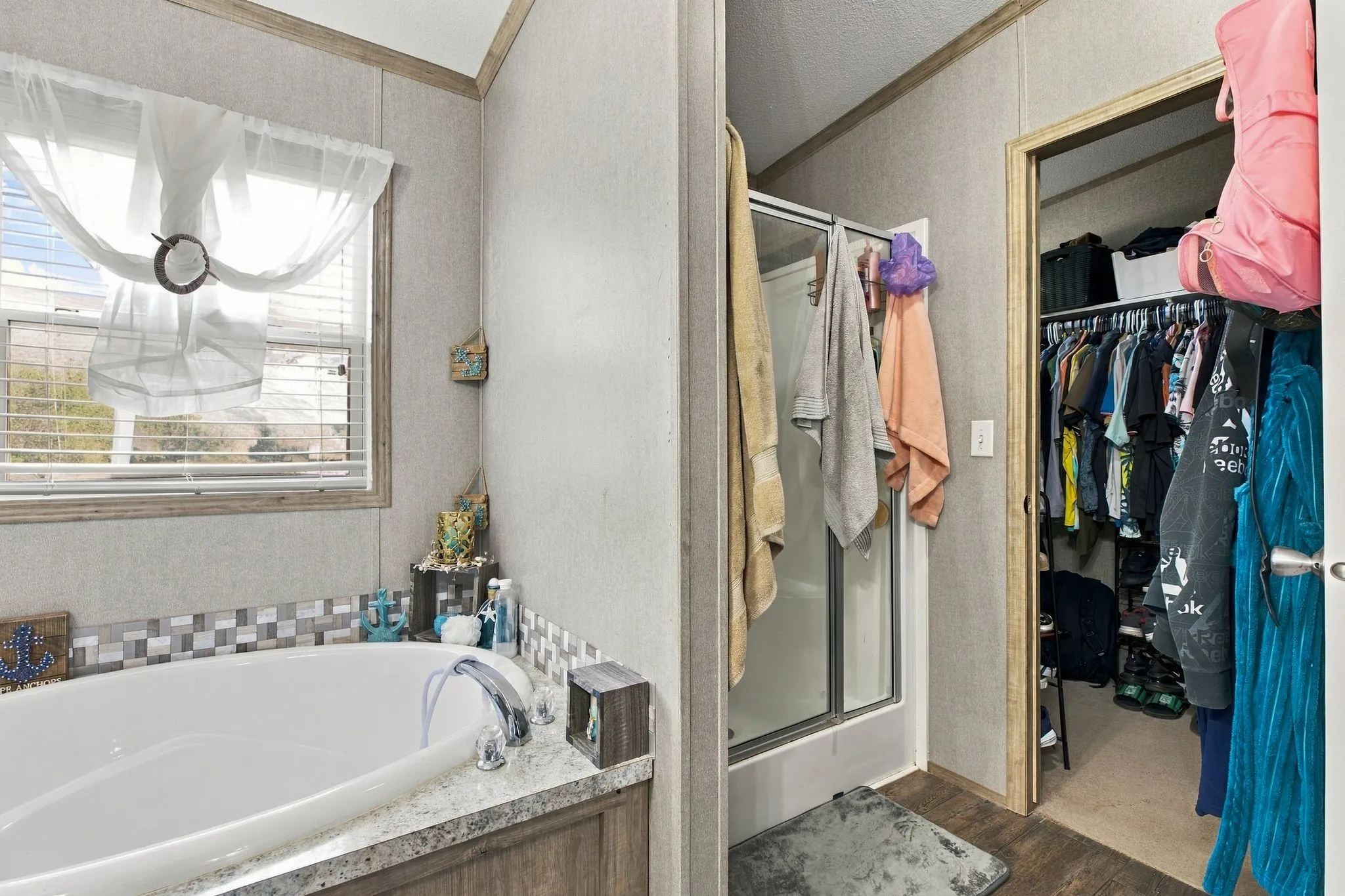 Bathtub with a mosaic tile backsplash, a window with blinds, a glass-enclosed shower, and wood-finish flooring