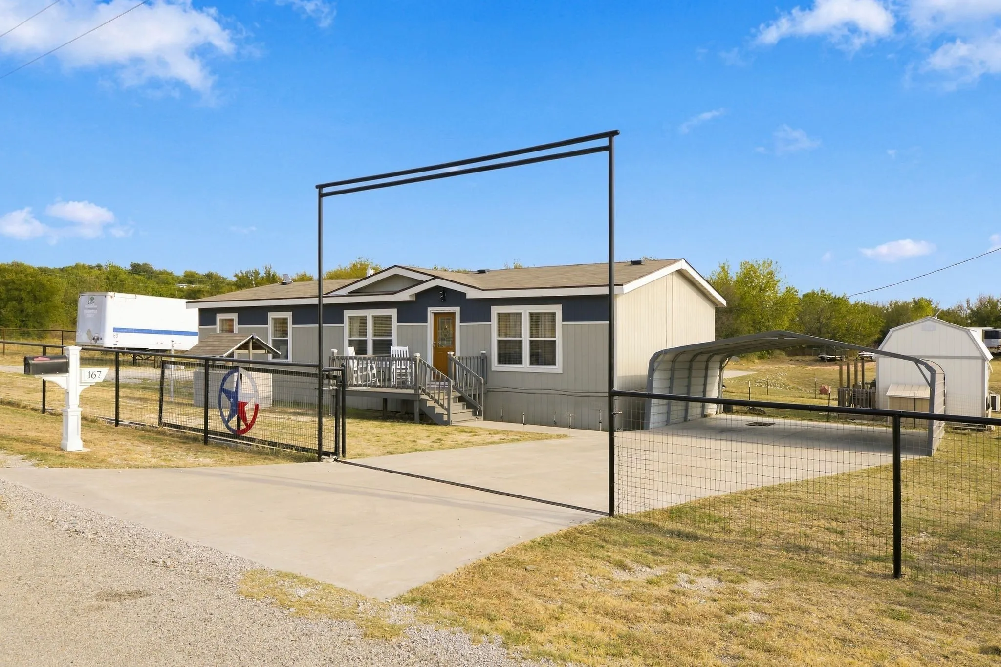 Two-tone exterior with covered front porch, gated entry, paved driveway, and detached covered parking structure
