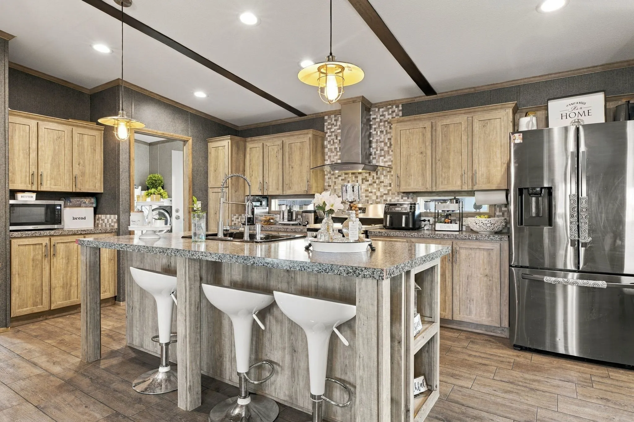 Kitchen featuring a large island with a stone-finish countertop, wood-finish flooring, light wood-tone cabinetry, stainless steel refrigerator, and a tiled backsplash