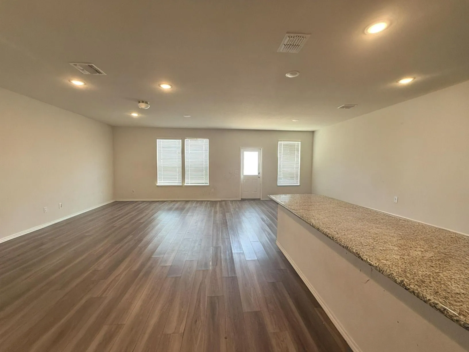 Spacious room with wood-finish flooring, recessed lighting, multiple windows with blinds, and a built-in counter with a speckled surface