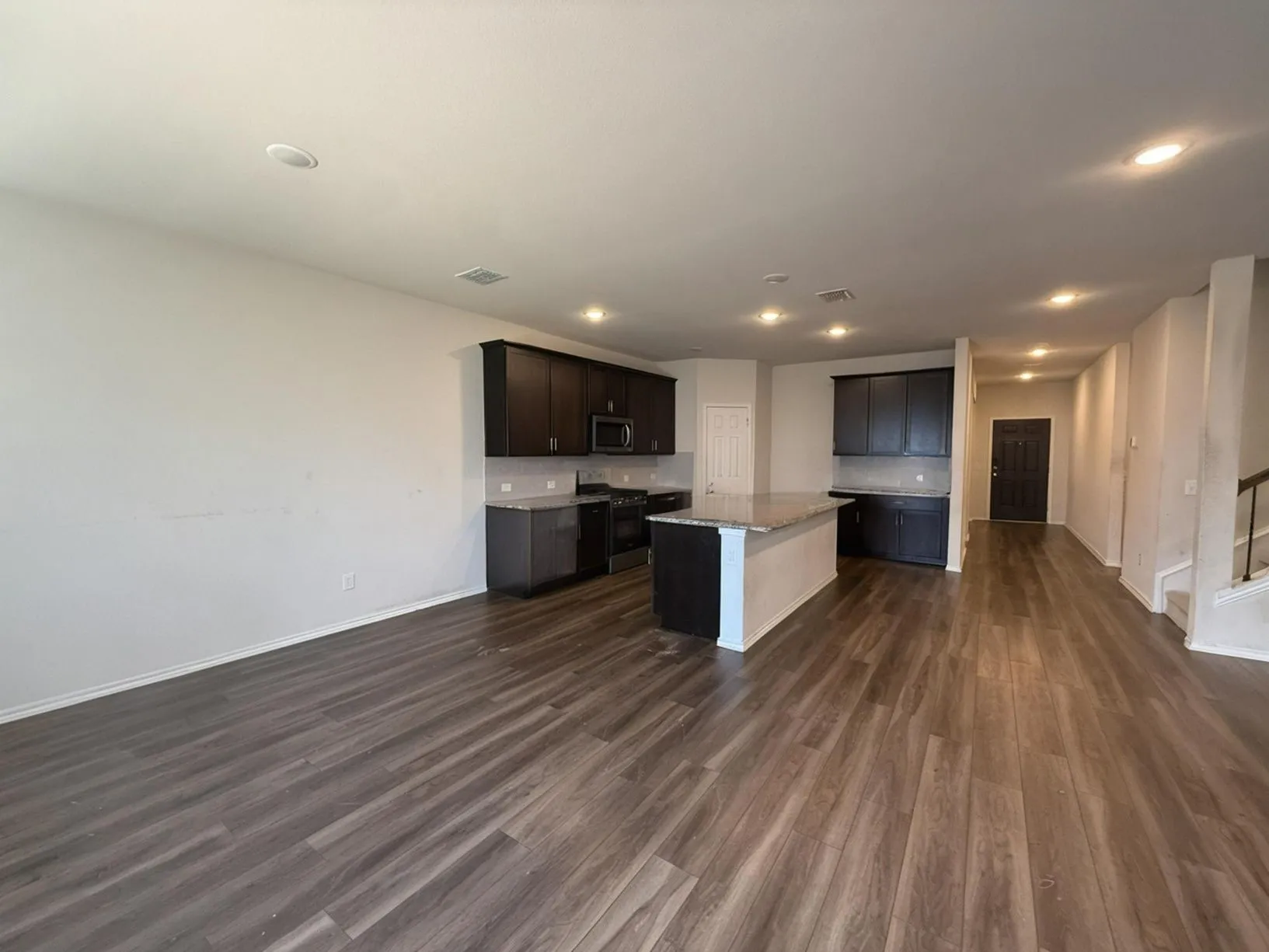 Open-concept living area featuring wood-finish flooring, recessed lighting, and a kitchen island with stone countertops