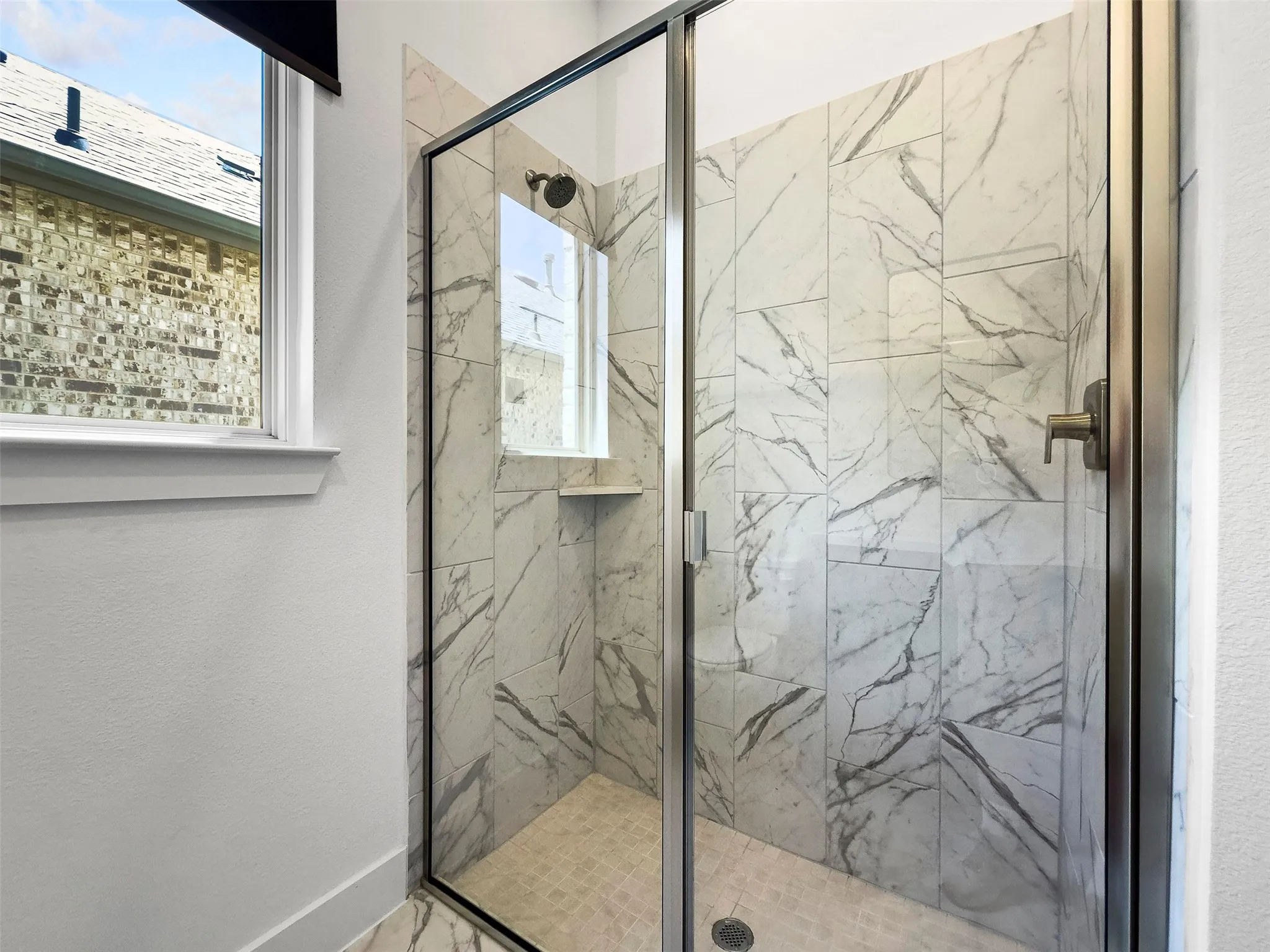 Frameless glass shower enclosure featuring marble-look wall tiling and a built-in shower niche
