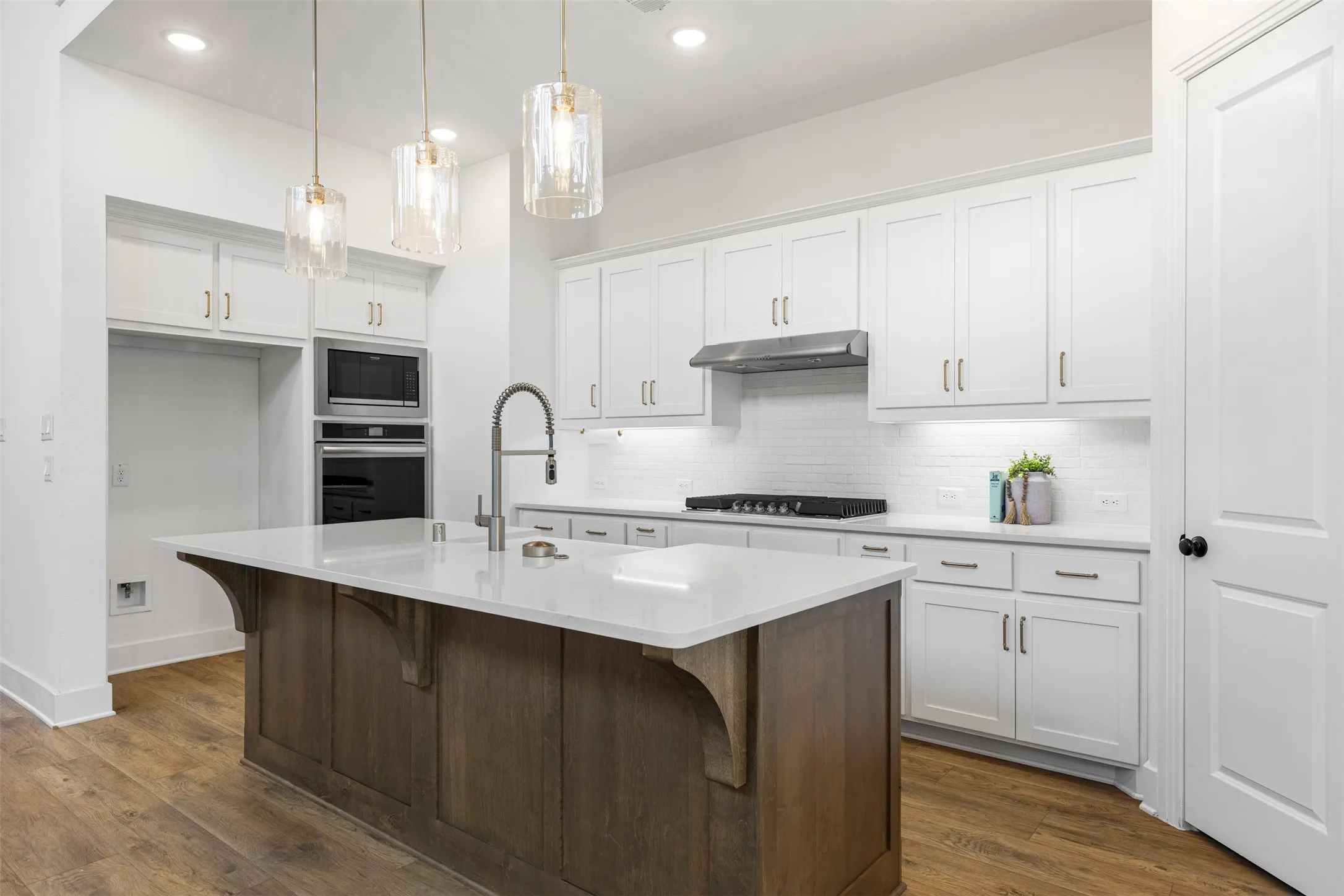 Kitchen featuring a central island with a light-toned countertop, wood-finish flooring, recessed lighting, and pendant light fixtures