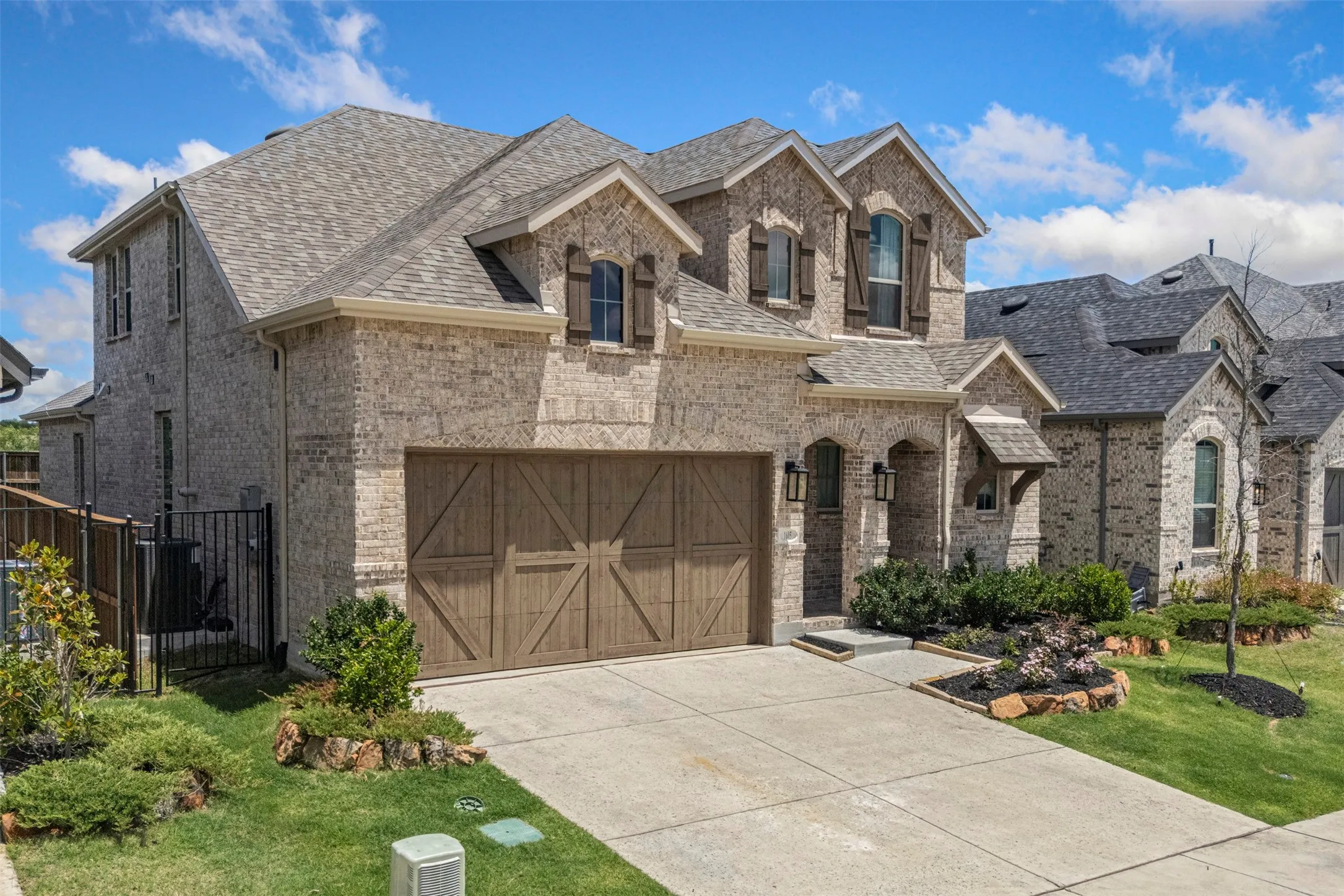 Brick exterior with stone accents, wood-finish garage door, arched entry, and mature landscaping