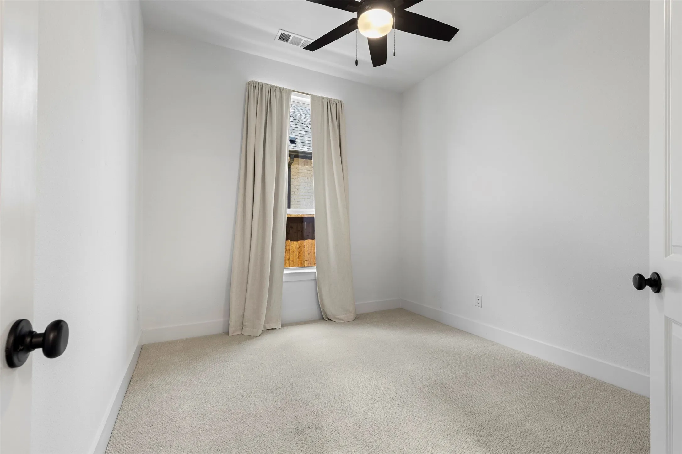Light-filled room featuring neutral carpeting, a black ceiling fan with integrated lighting, and a window with custom drapery