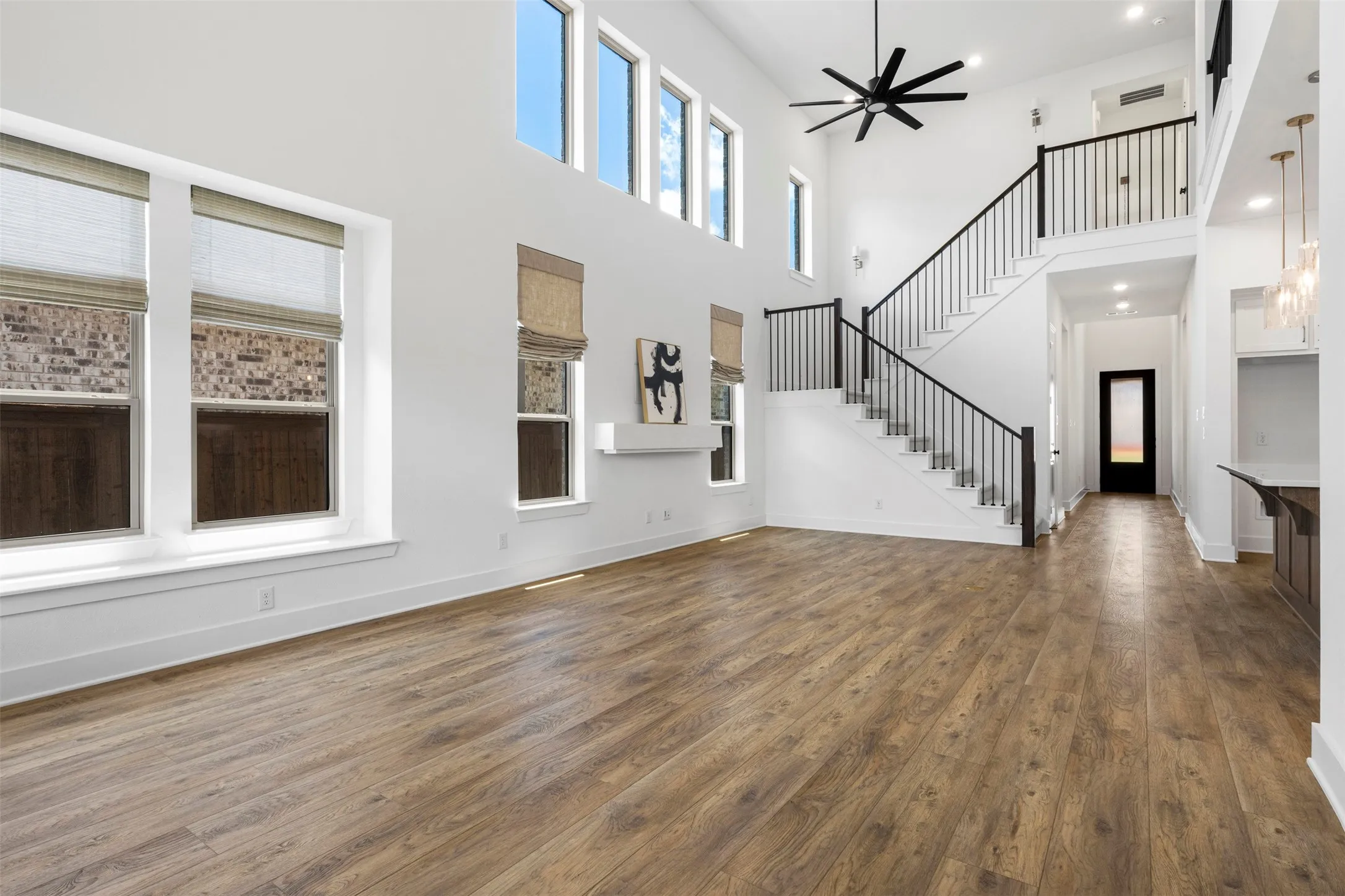 Vaulted ceiling with a large ceiling fan, wood-finish flooring, and a staircase featuring black metal balusters