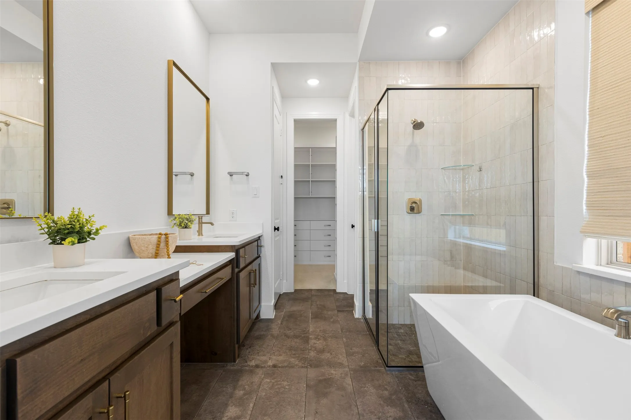 Dual vanity with white countertops, wood-finish cabinetry, and gold-framed mirrors