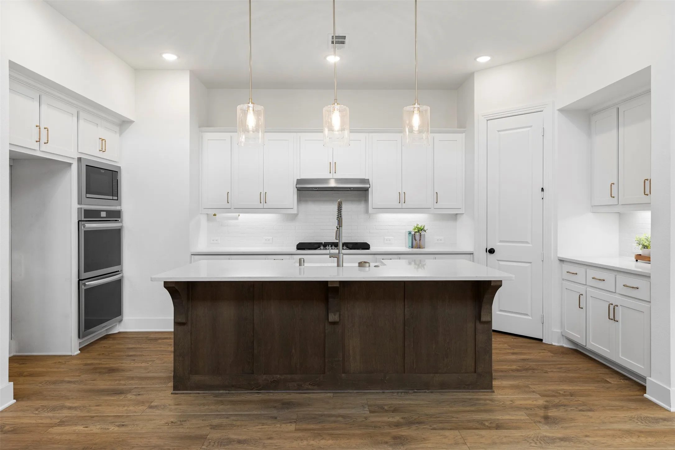 White cabinetry, wood-finish flooring, central island with seating, stainless steel appliances, and pendant lighting