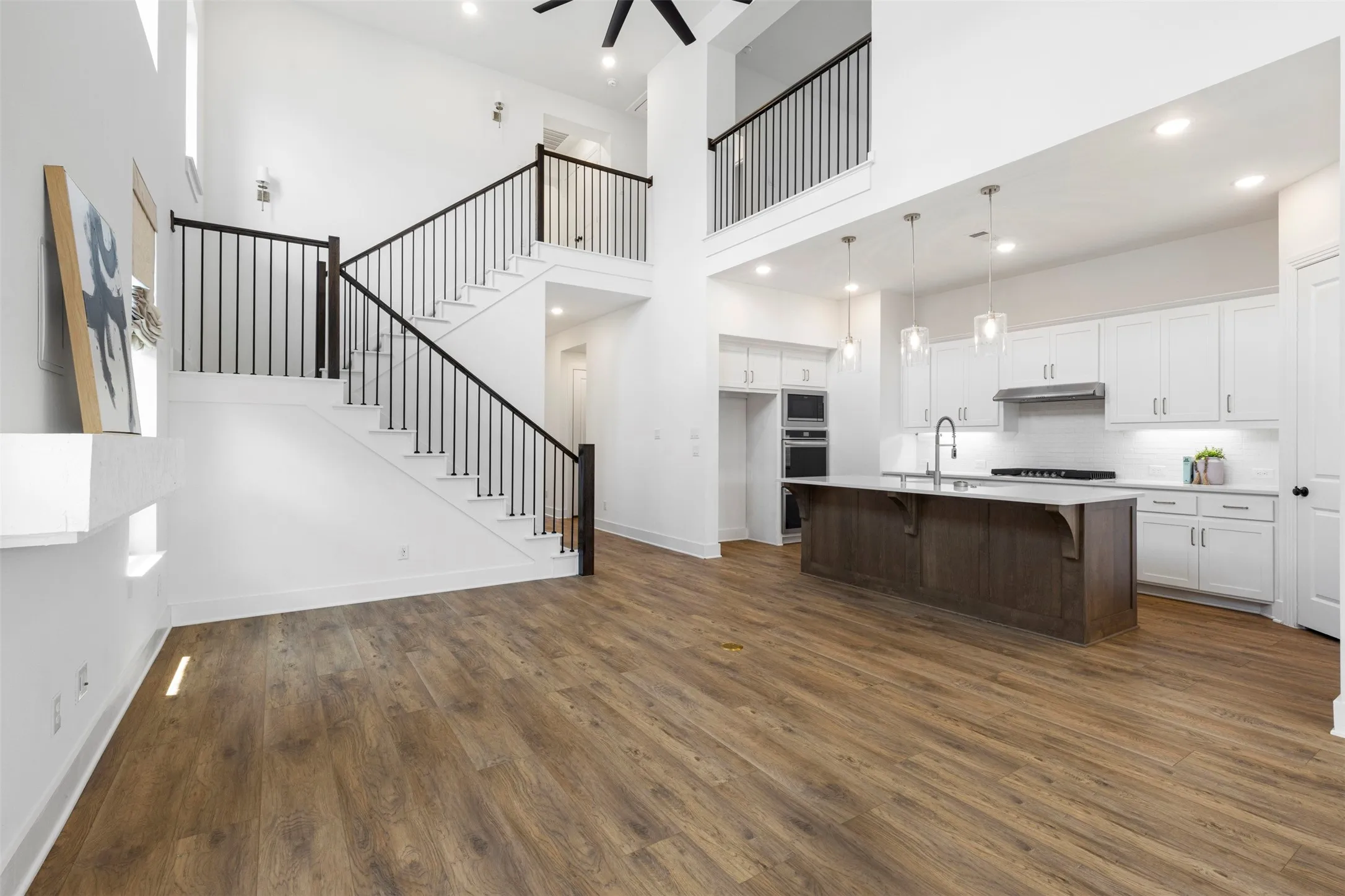 Expansive open-concept living area featuring wood-finish flooring, a two-story ceiling, and a modern kitchen