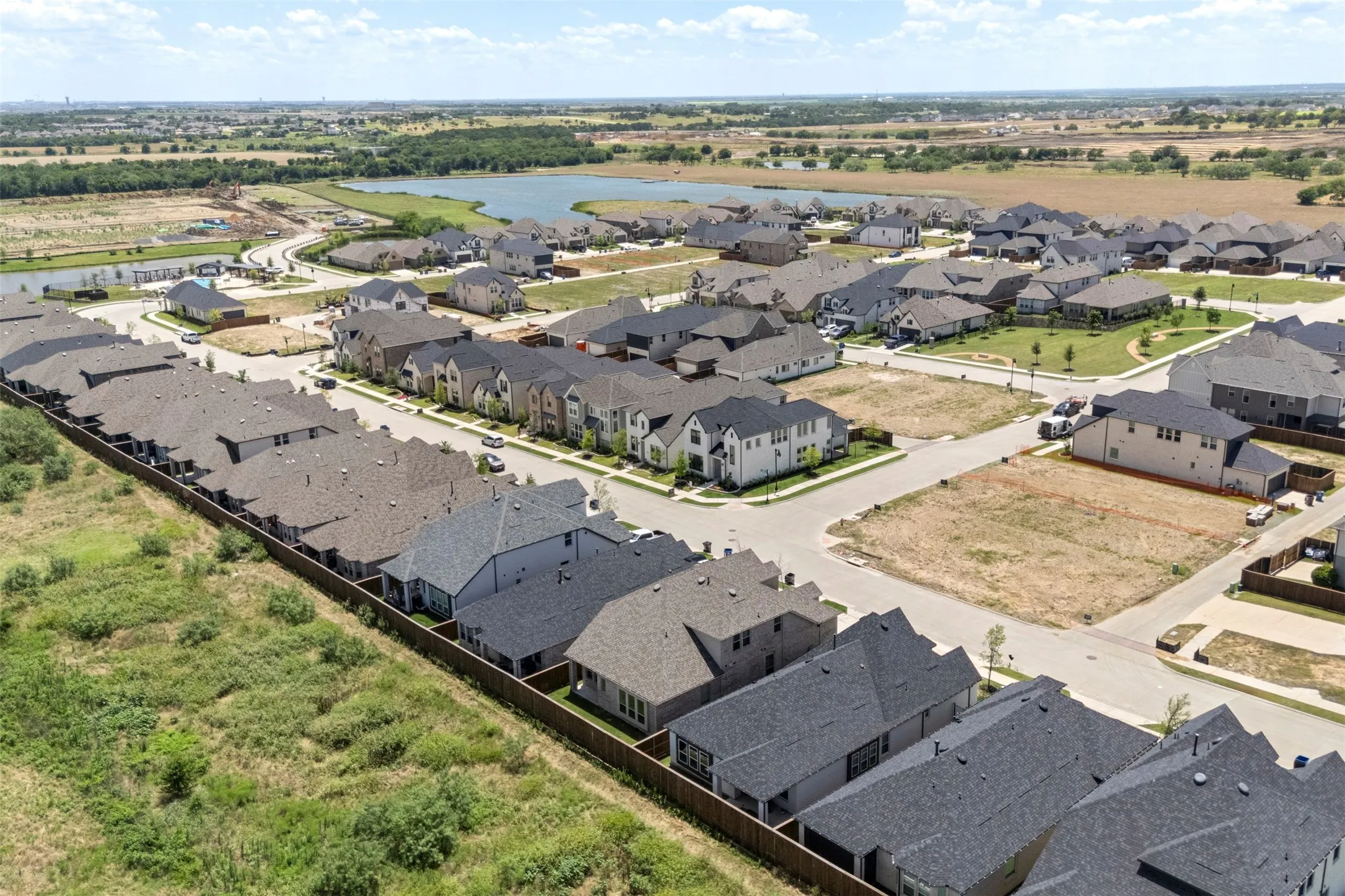 Aerial perspective showcasing a developing residential community, multiple single-family homes with varying rooflines, and undeveloped lots