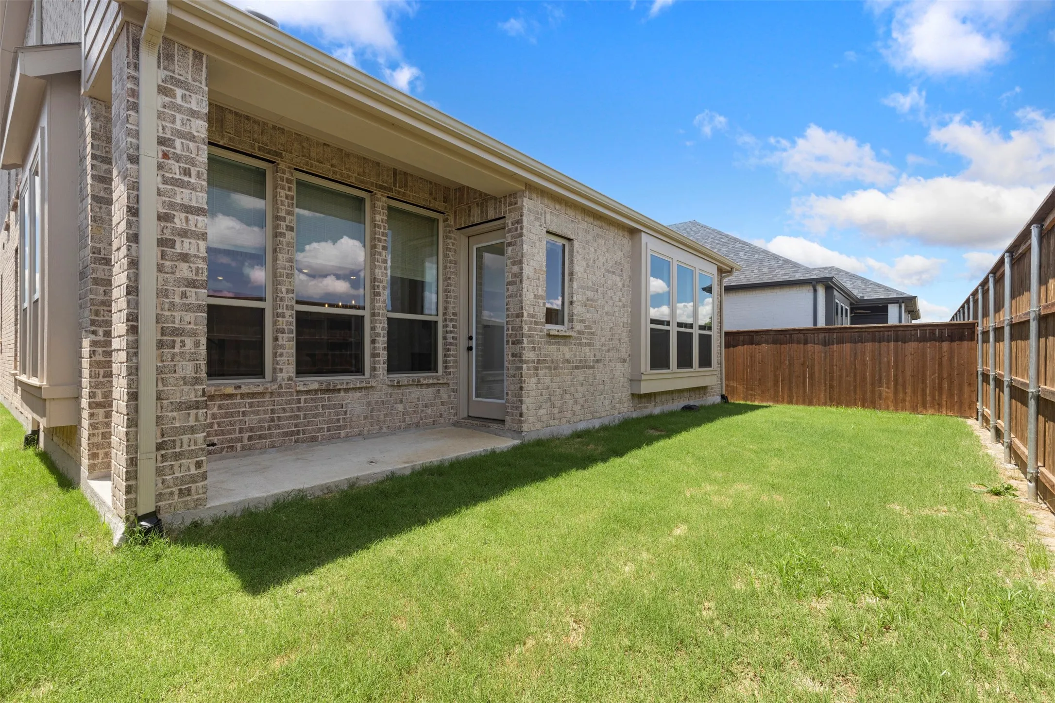 Expansive backyard with a covered concrete patio, wood privacy fencing, and a bay window feature
